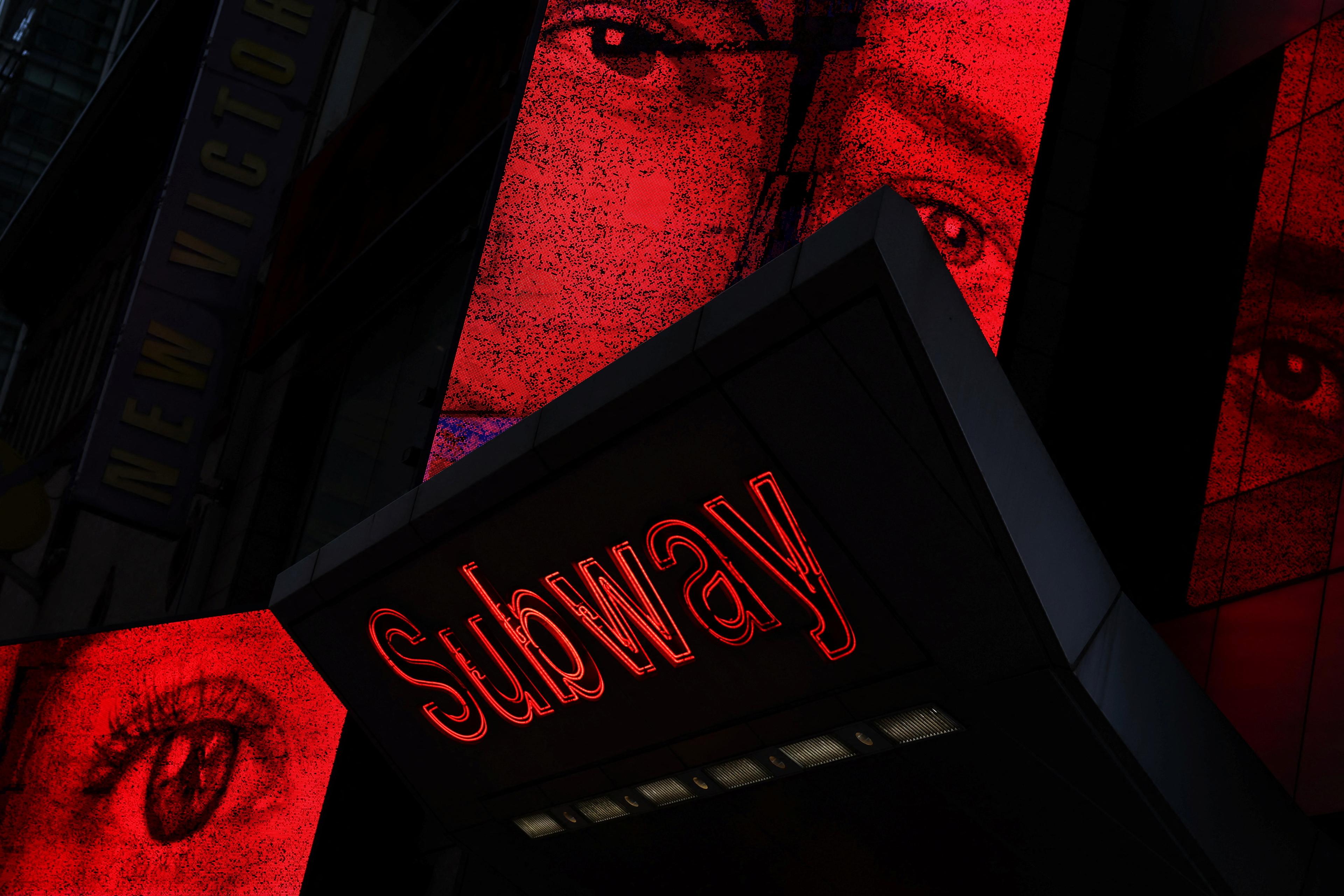 A subway sign with red neon text and large images of eyes on illuminated red panels above.