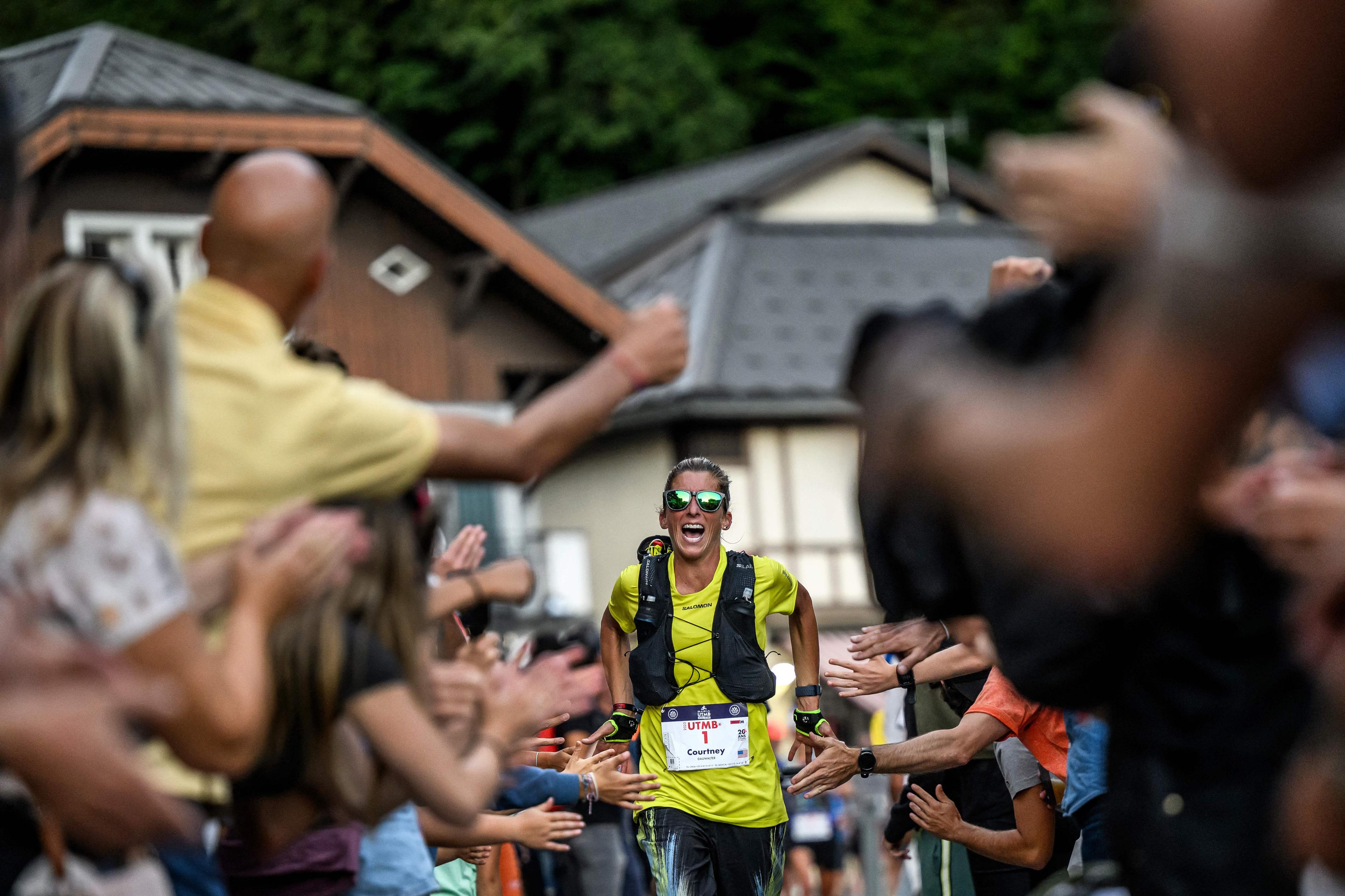 A smiling runner in a yellow shirt high-fiving a cheering crowd on a street lined with buildings and trees.