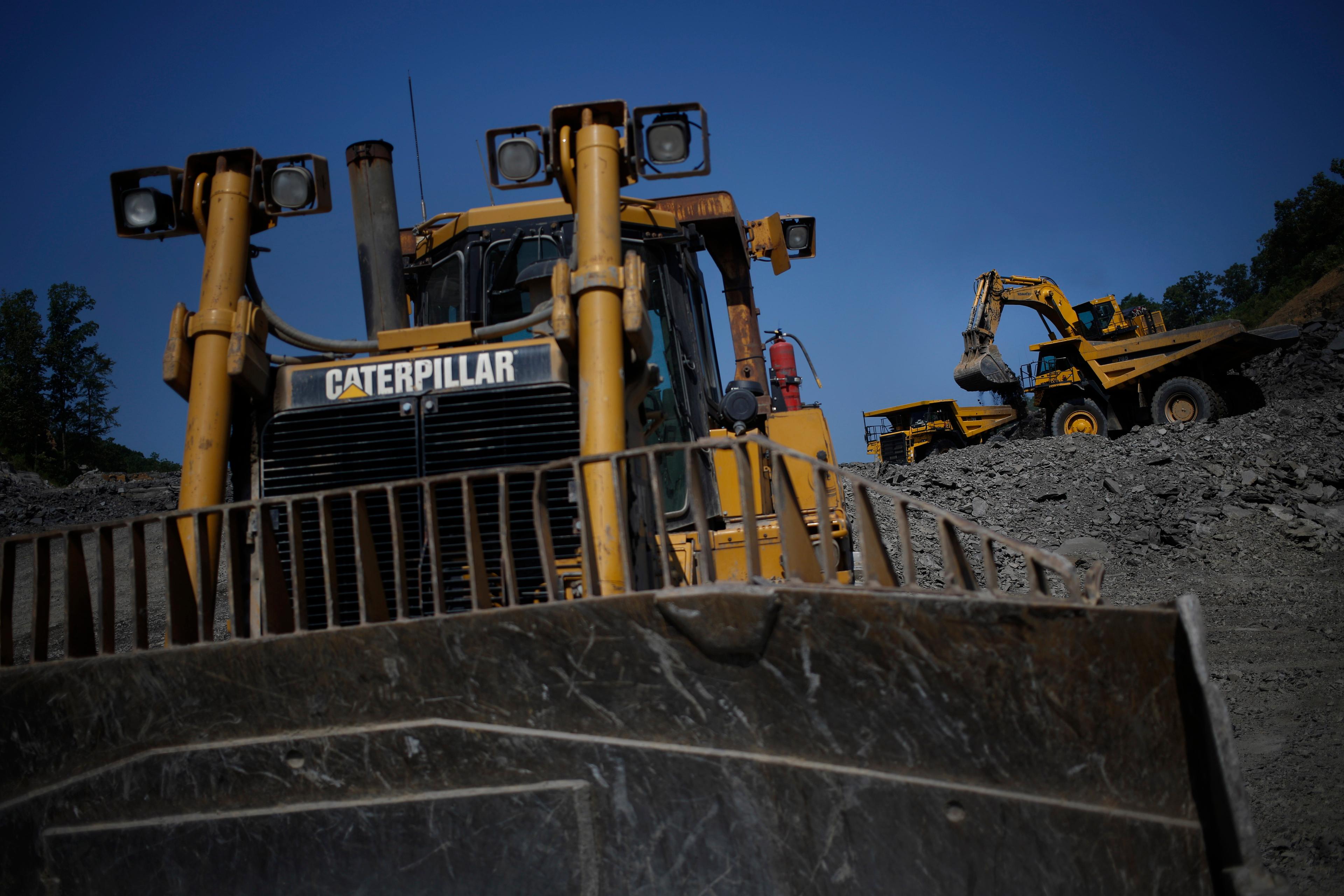 A bulldozer and excavator at a quarry with a clear blue sky in the background.