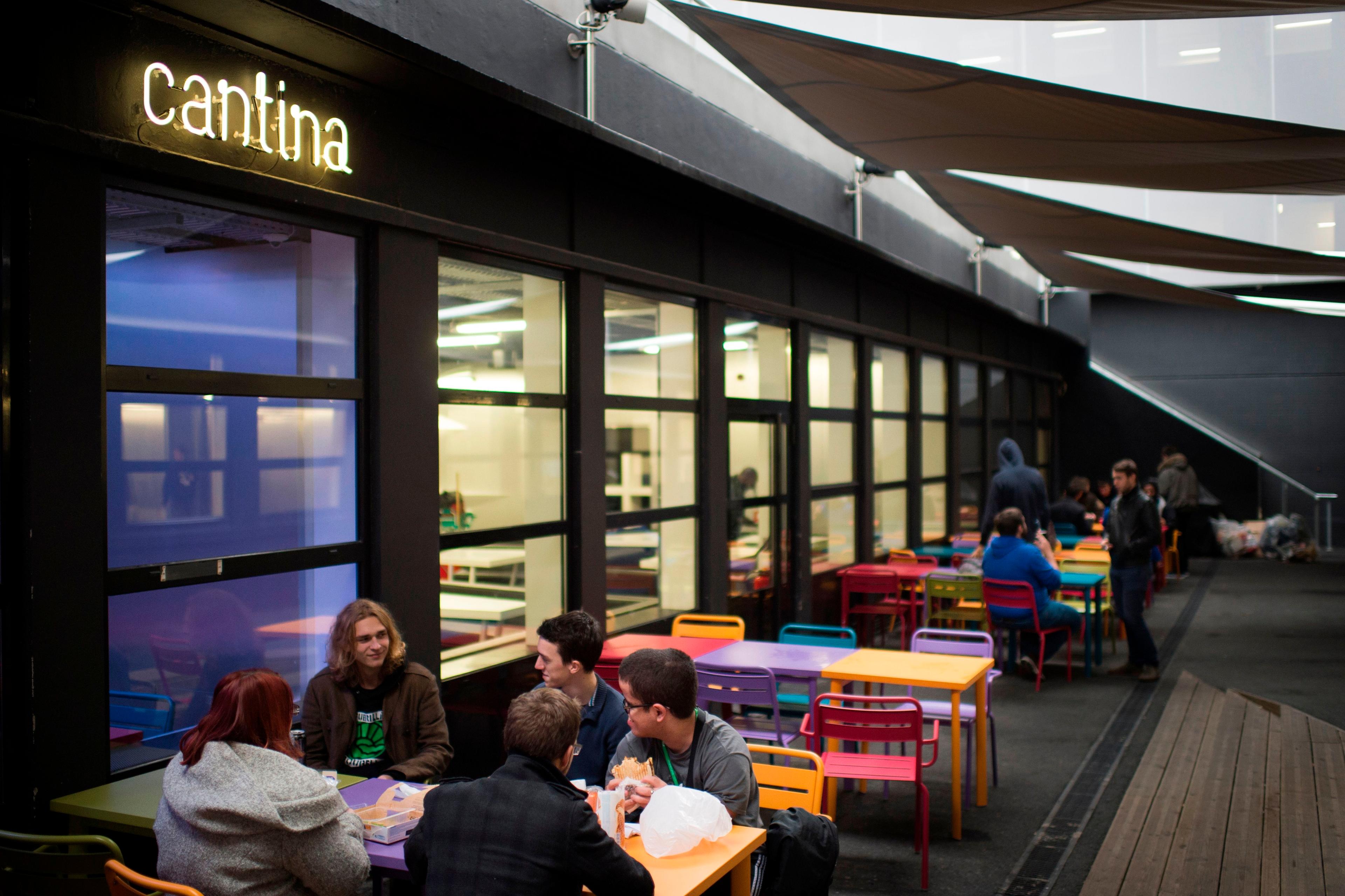 Photo of a cantina with people sitting at colourful tables outside under a canopy.