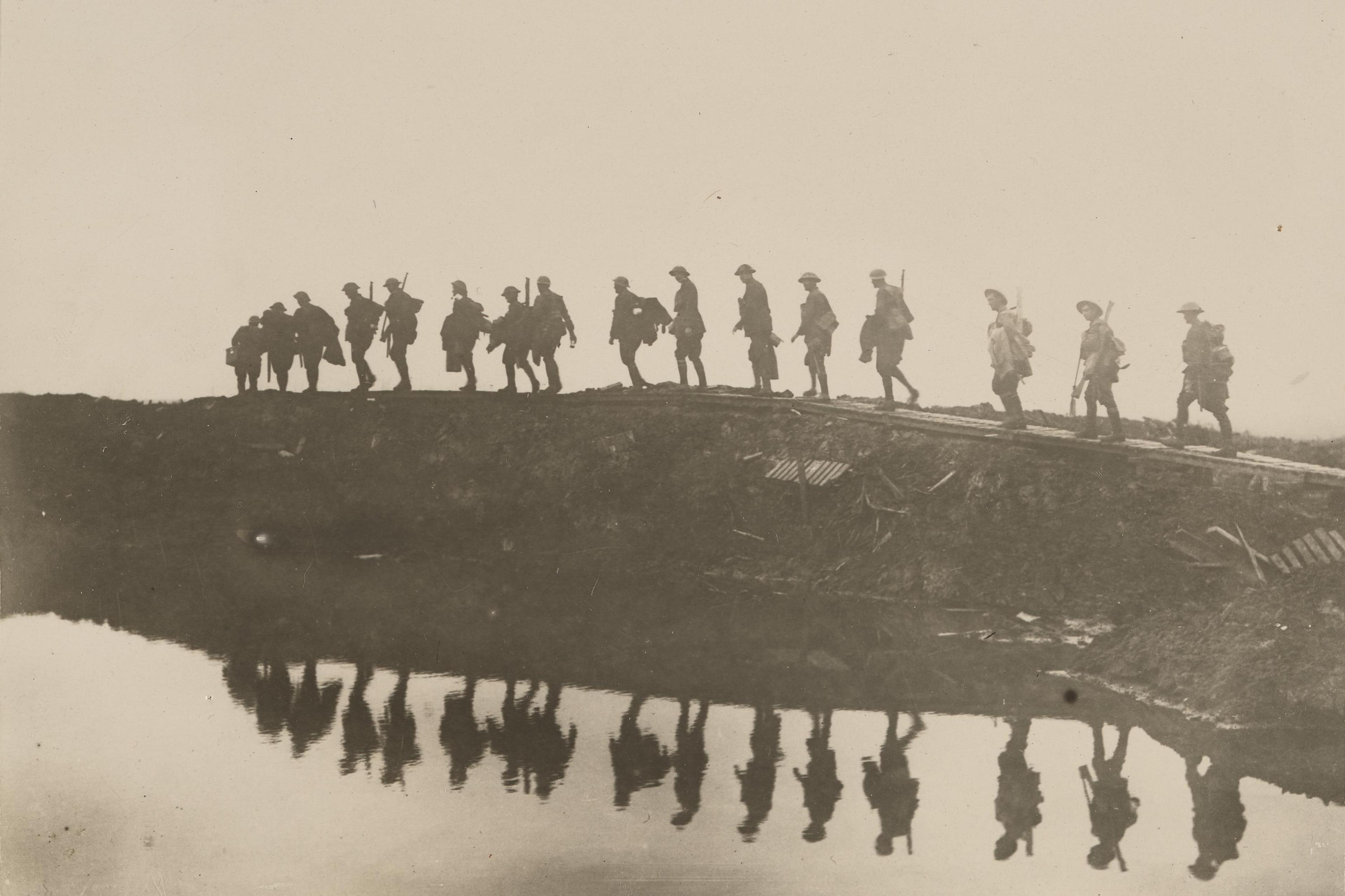 Black and white photo of soldiers walking on a ridge with their reflections in the water below.
