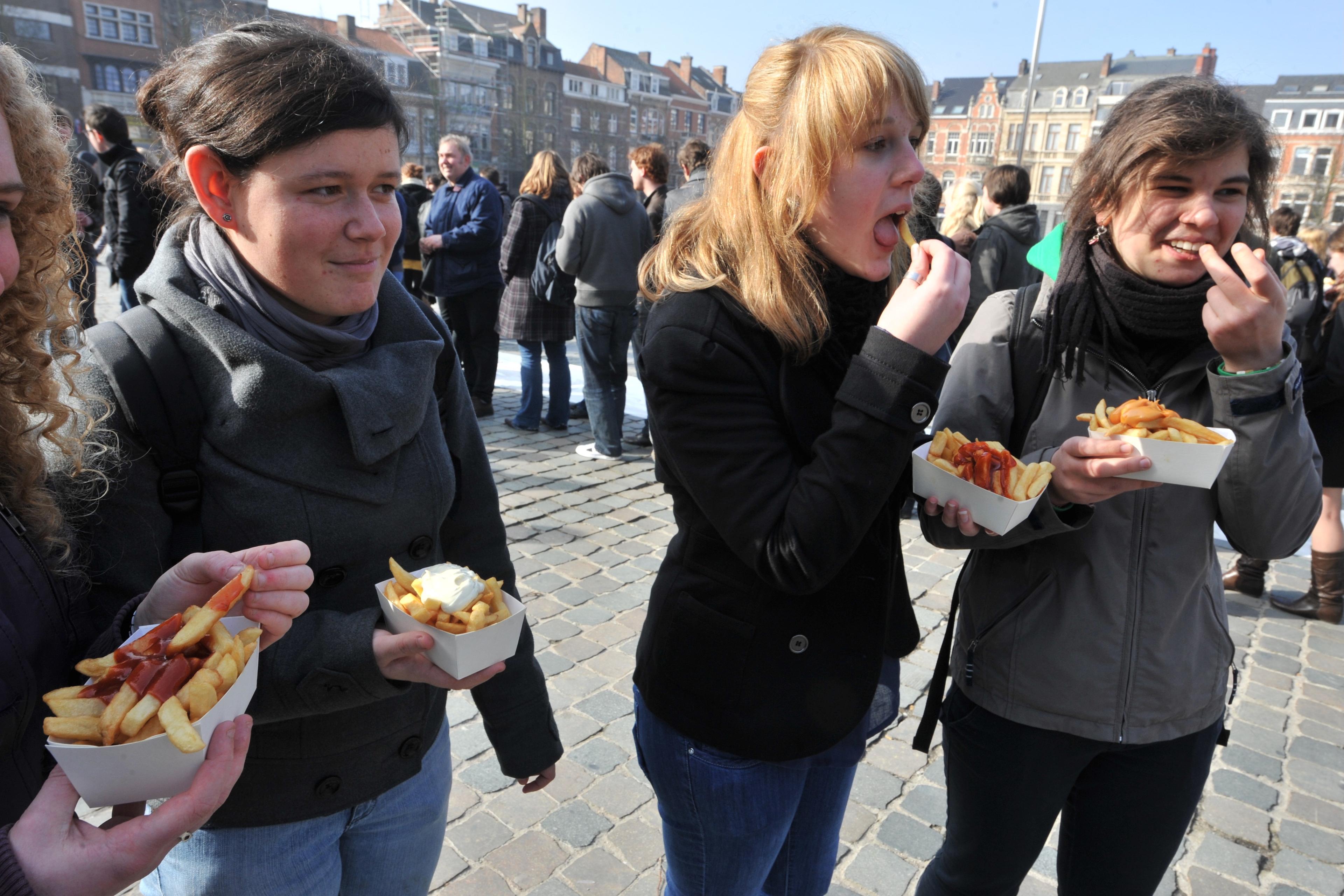 Photo of four people outdoors eating chips with sauce from trays on a cobblestone street with buildings in the background.