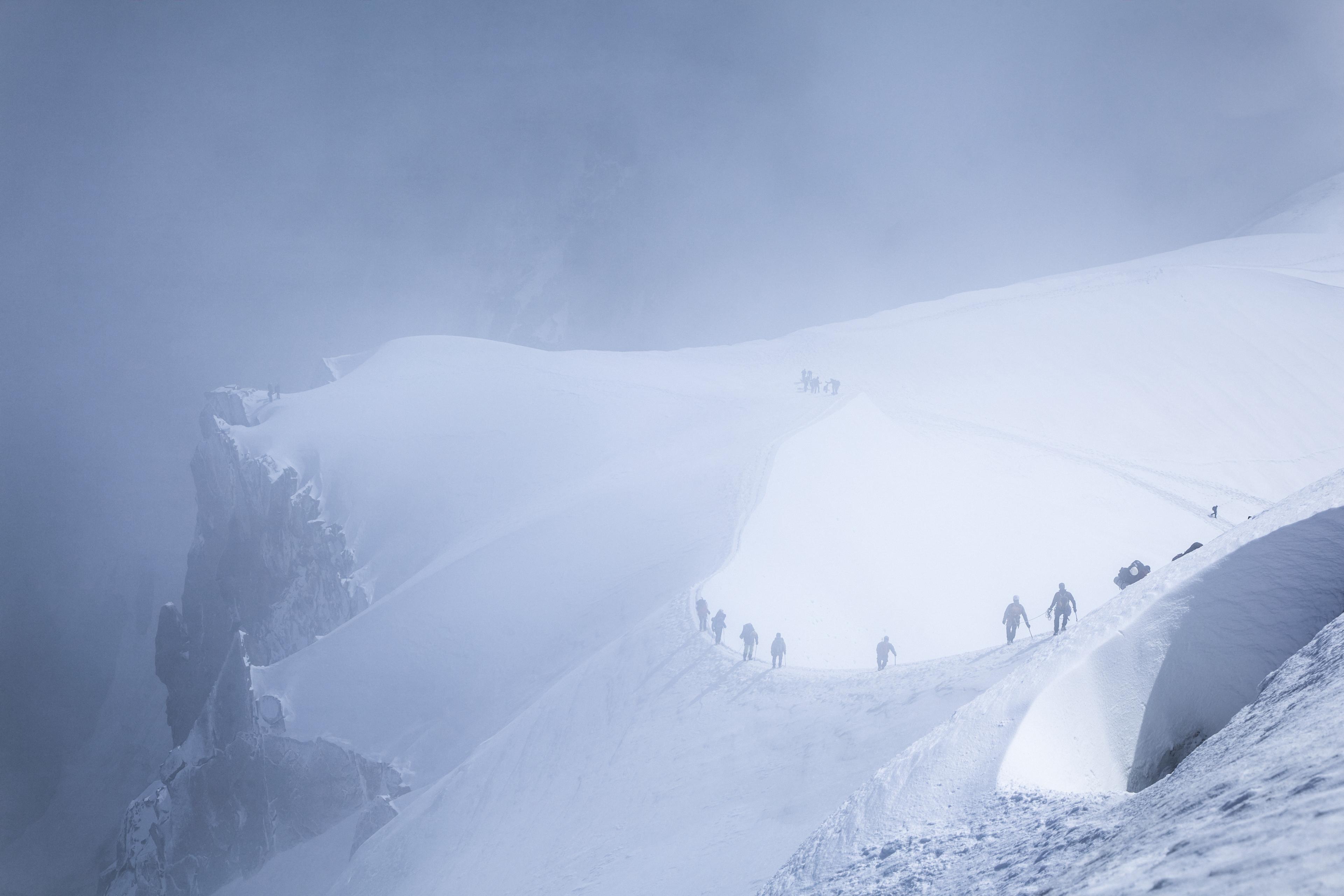 Photo of climbers trekking on a snow-covered mountain ridge shrouded in mist and clouds.