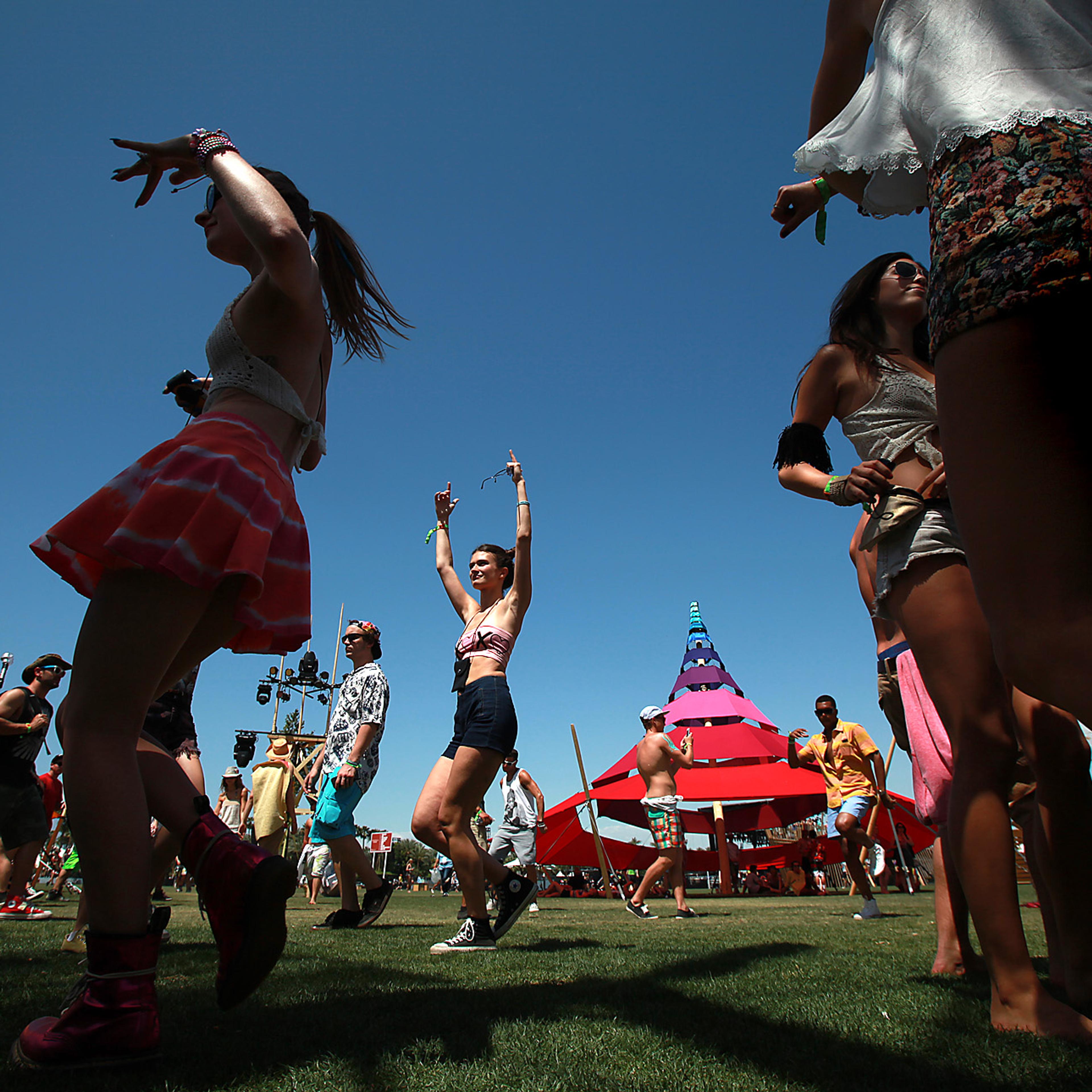 People dancing at an outdoor festival, colourful tents in background, clear blue sky overhead.