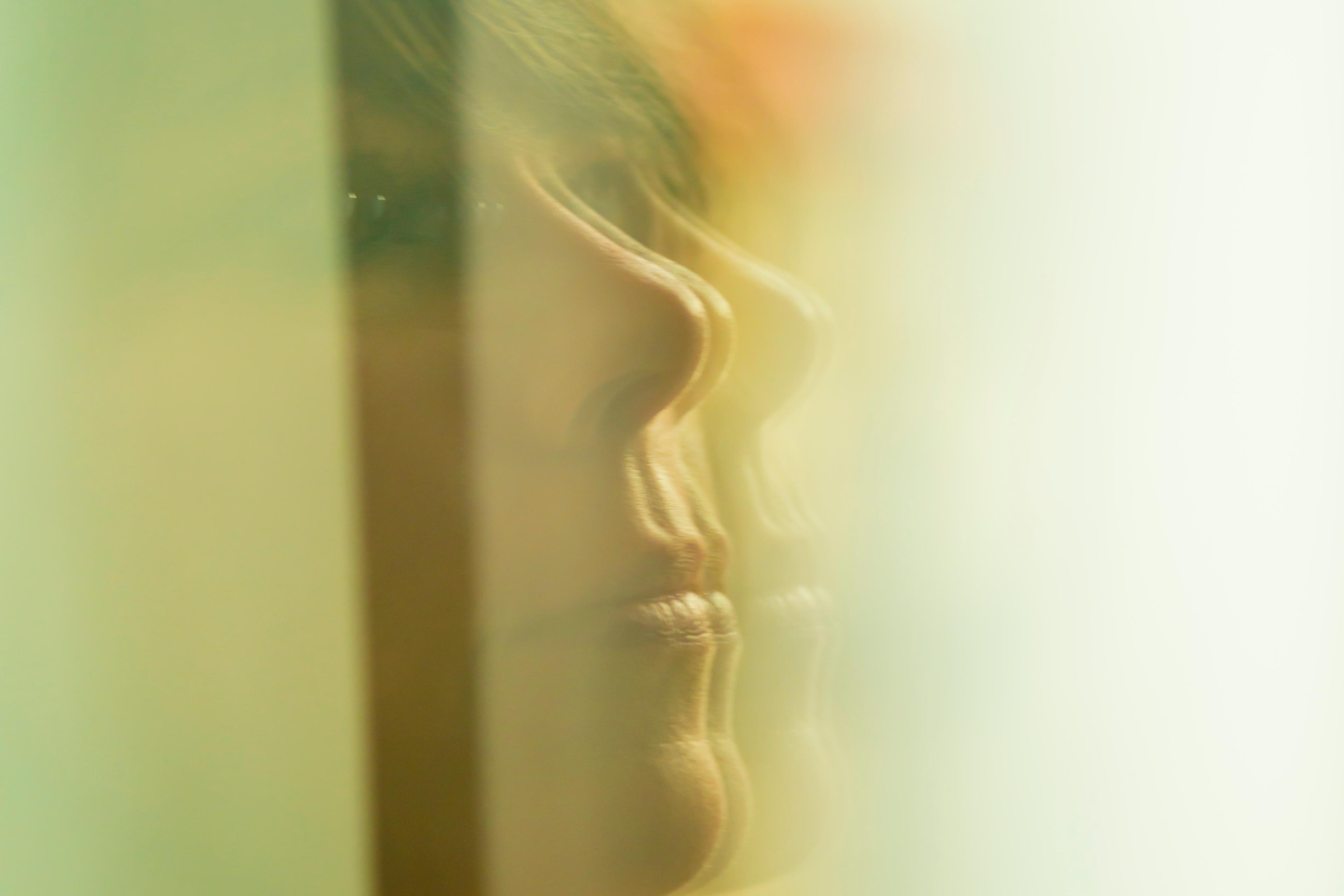 Photo of a woman’s face reflected in a glass window with soft, abstract focus and greenish tones.