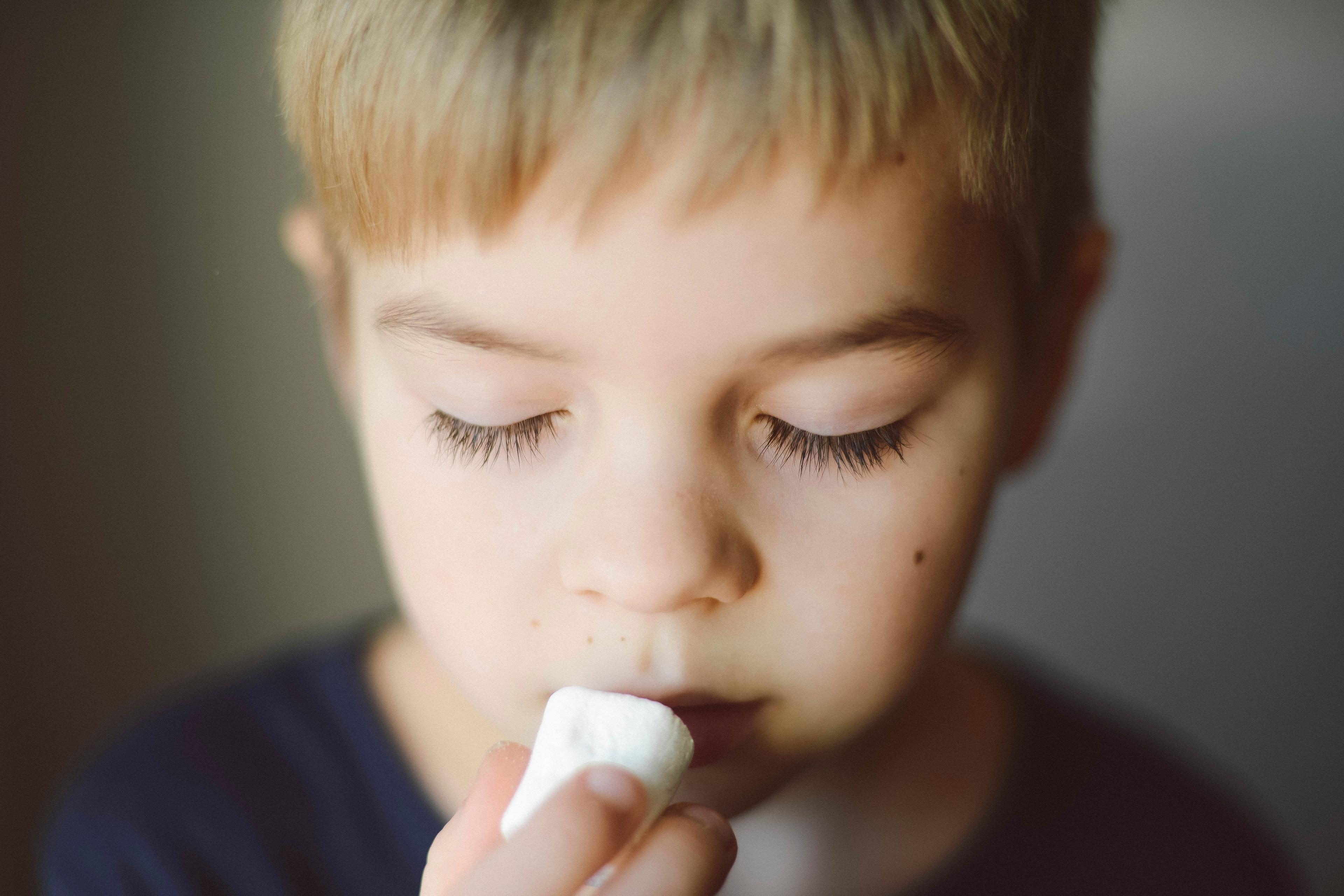 Photo of a young child holding a marshmallow close to their mouth eyes closed in contemplation.