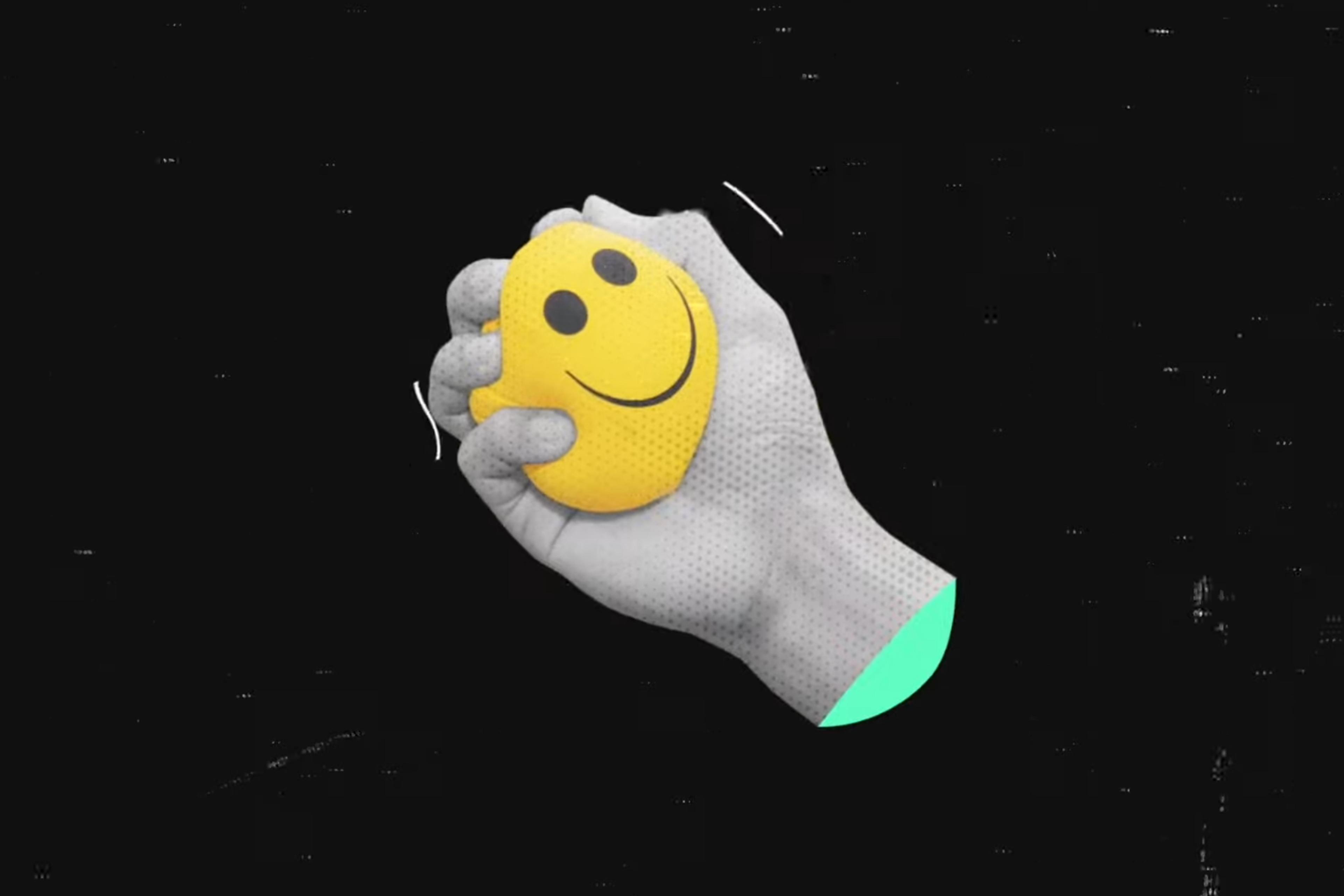 Digital artwork of a grey hand squeezing a yellow stress ball with a smiley face on a black background.