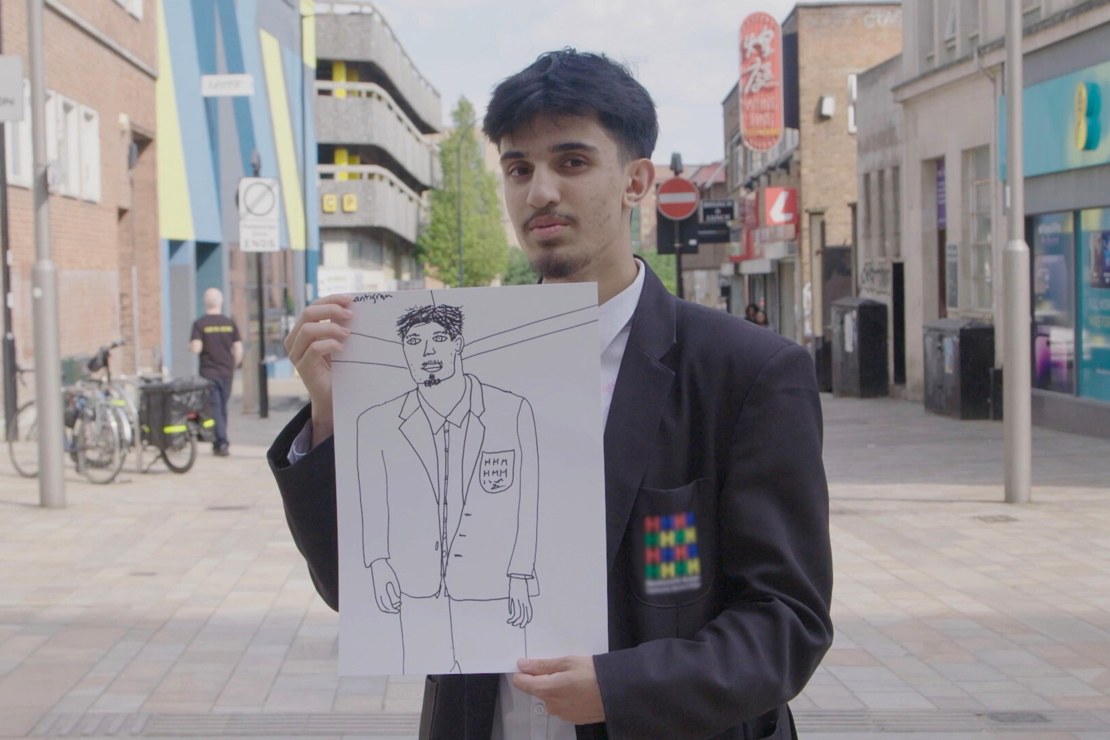 Photo of a man holding a hand-drawn sketch of himself on a city street, wearing a blazer with a colourful patch.