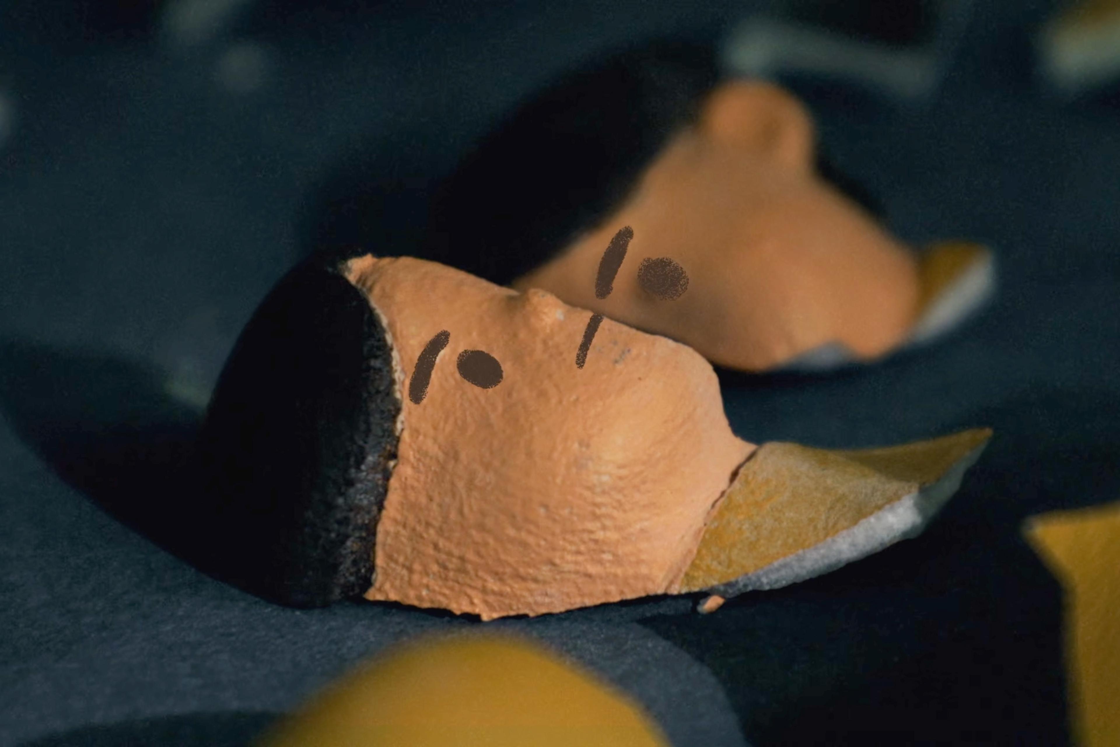 Two clay faces with minimal features lying on a dark surface in a close-up photograph.