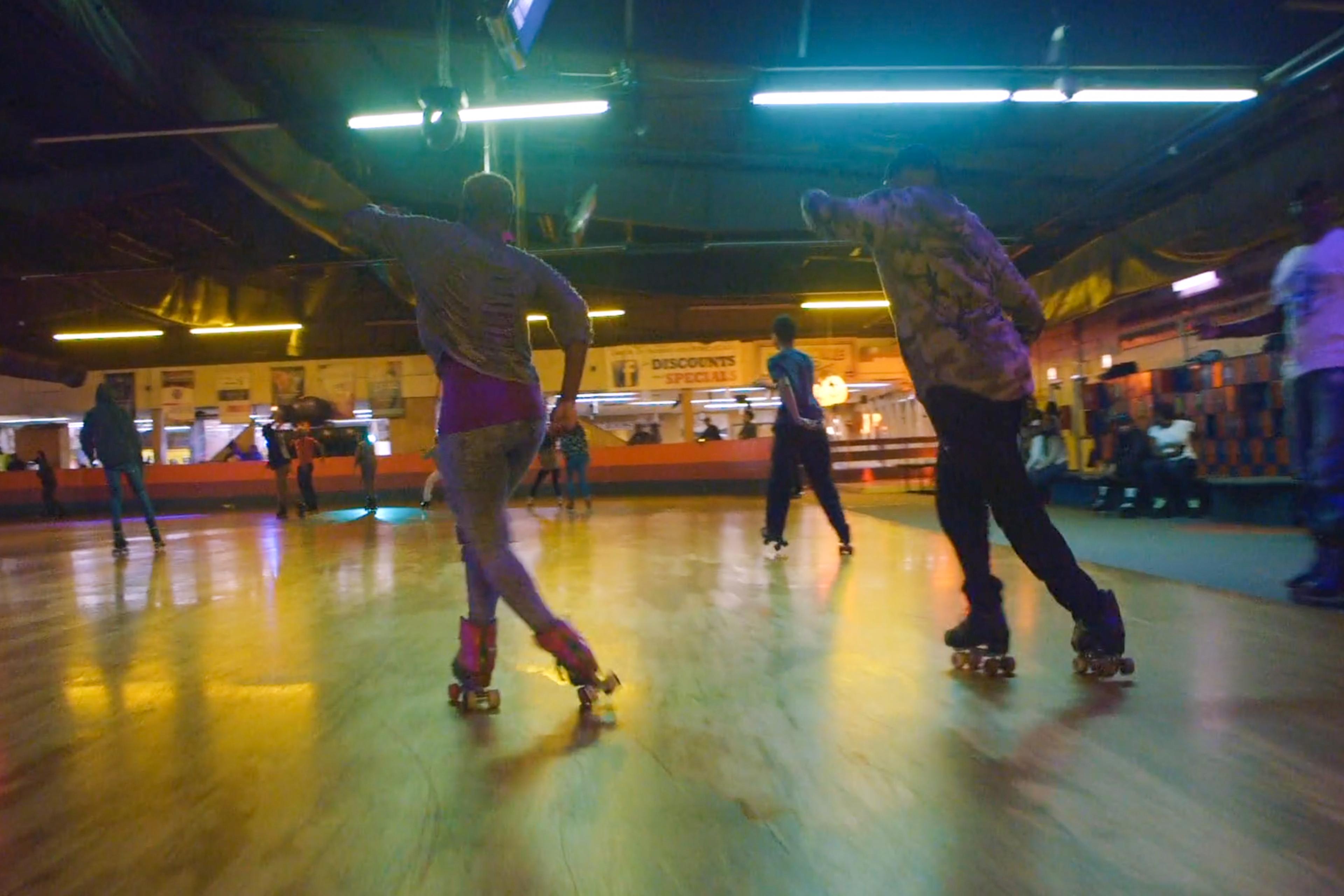 Photo of people roller skating on a wooden rink under neon lights in an indoor facility.