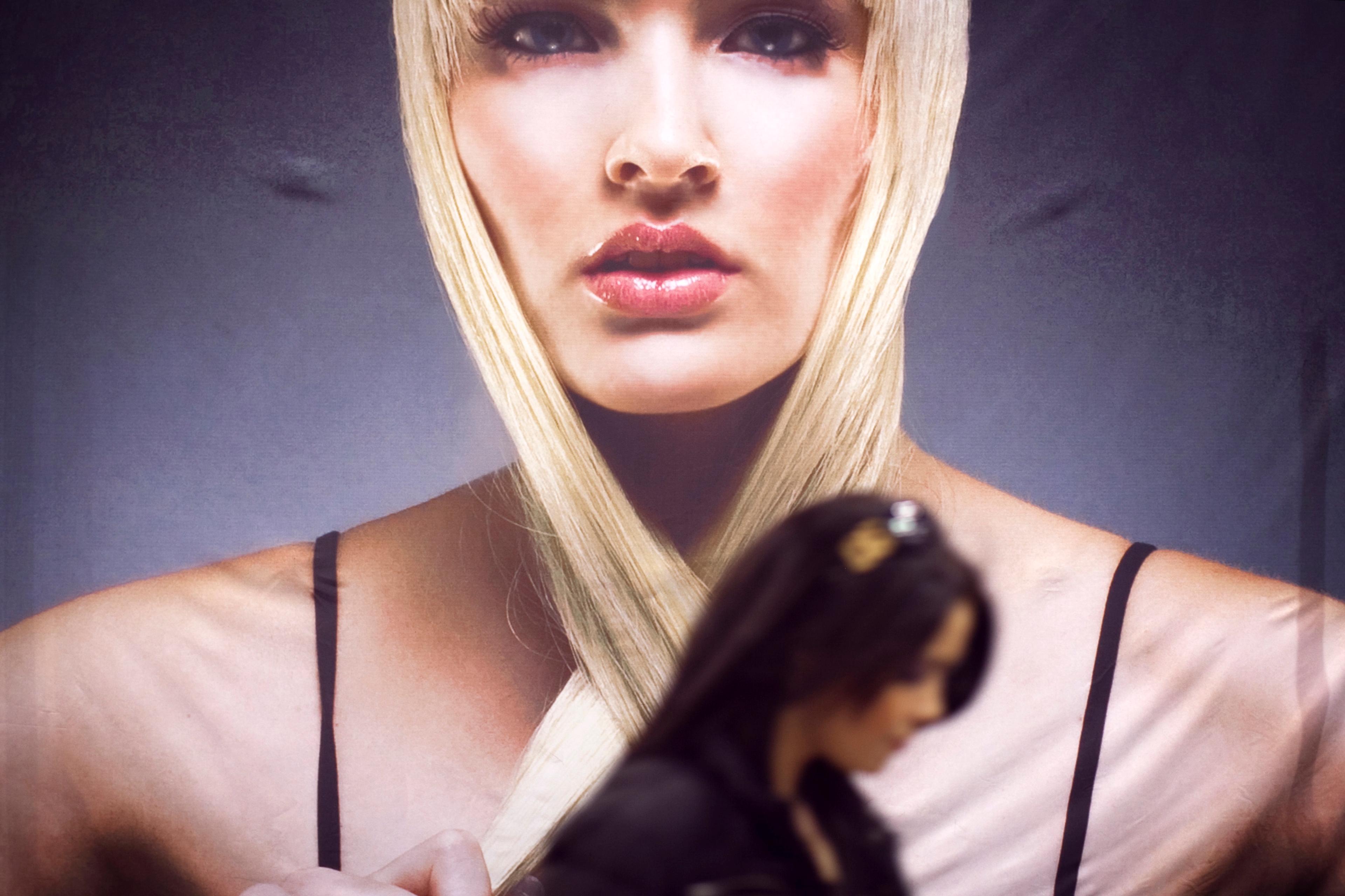 Photo of a large poster depicting a woman with blonde hair, with a person walking in the foreground.