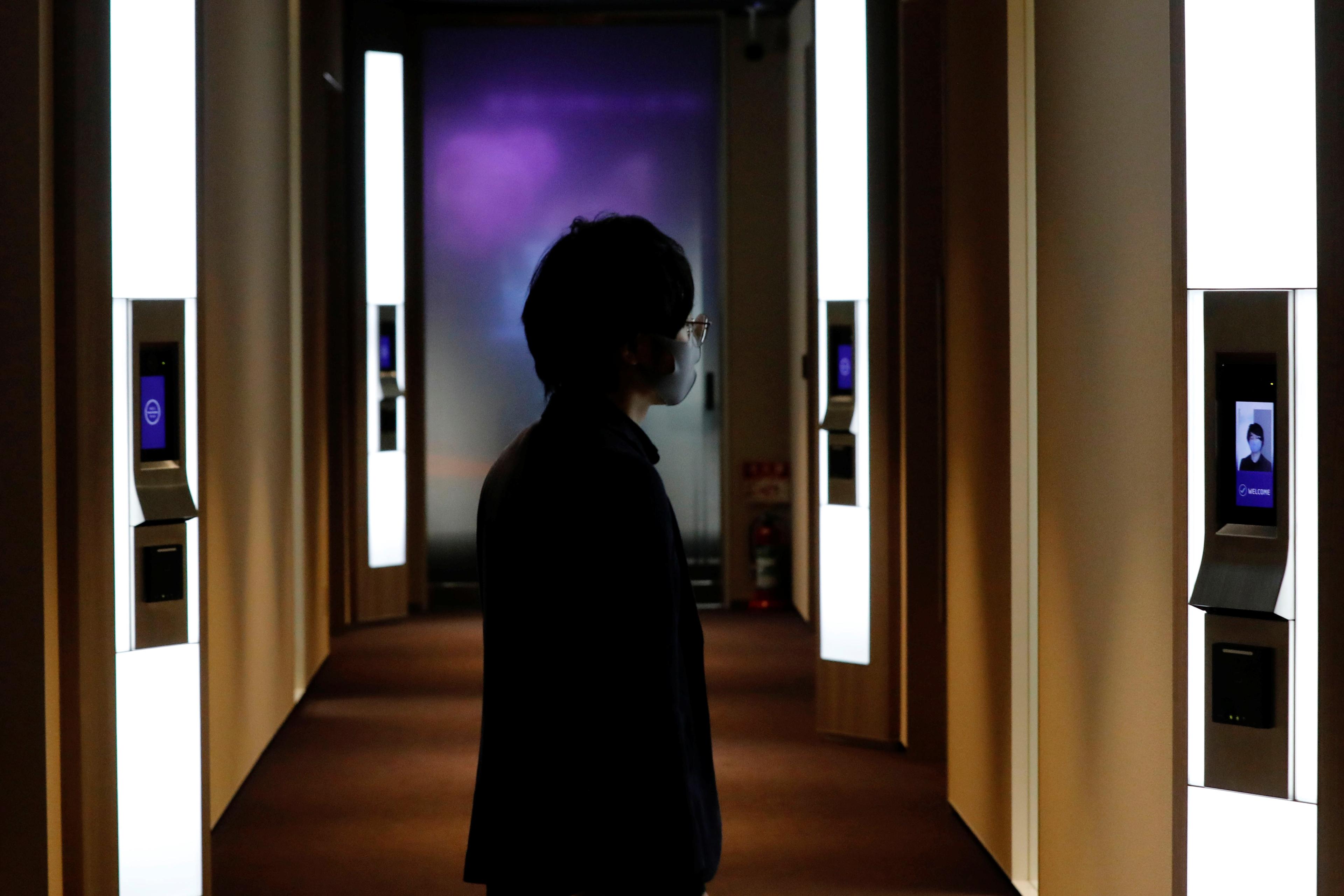 Photo of a person using facial recognition in a dimly lit hallway with illuminated screens on the walls.