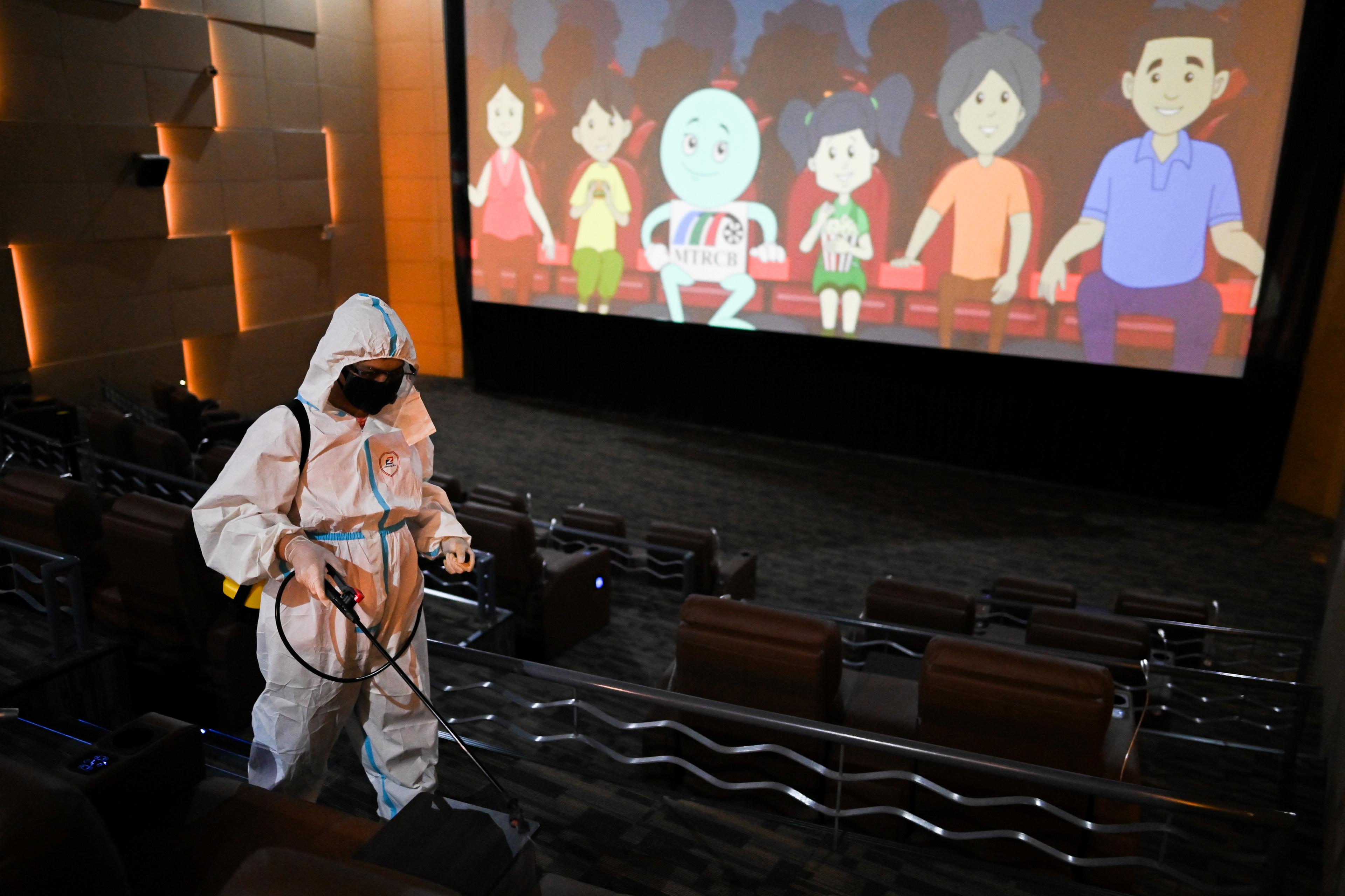 Photo of a person in protective gear disinfecting an empty cinema with an animated film playing on the screen.