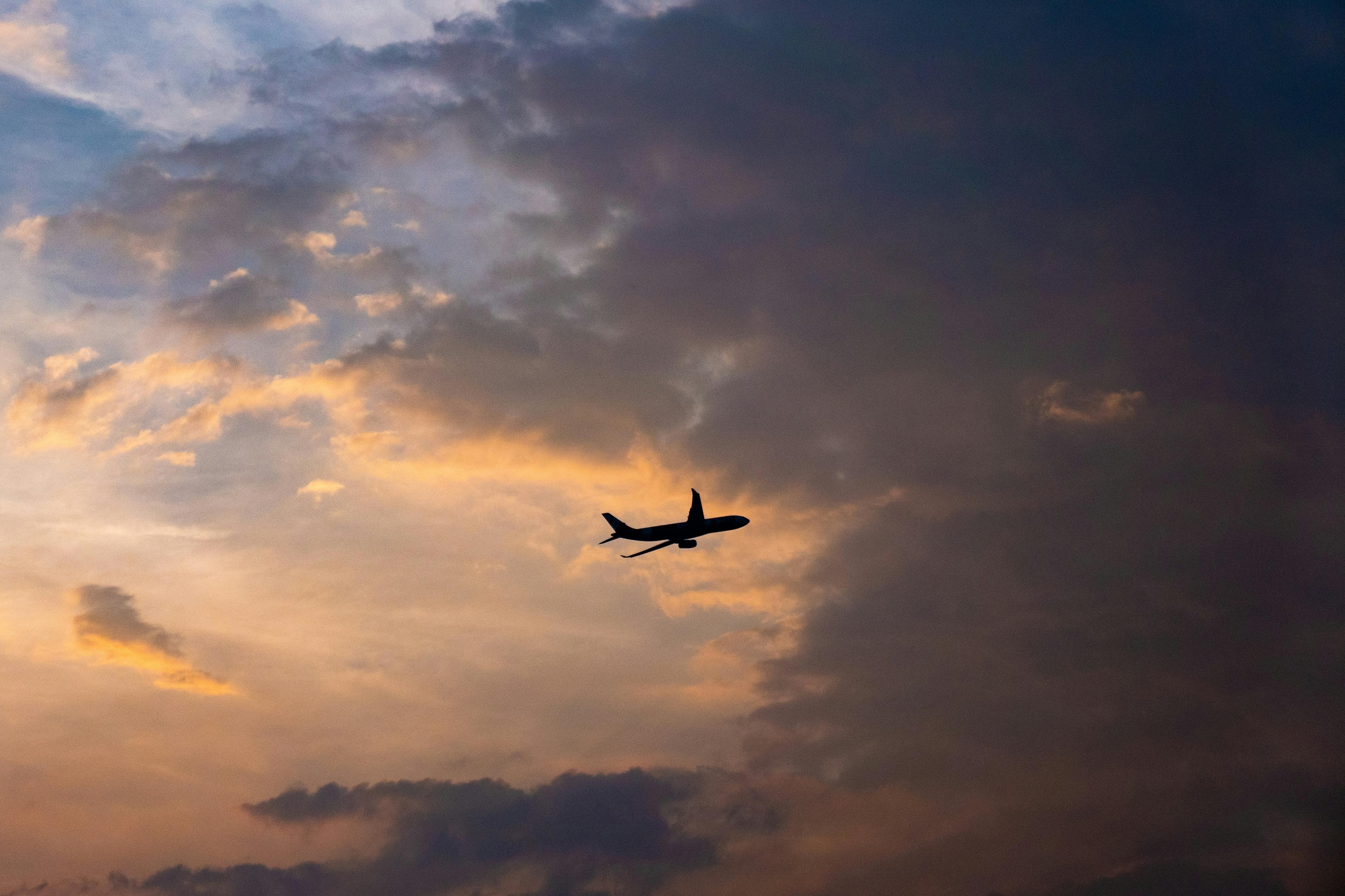 An aeroplane seen in silhouette, flying against a dramatic sunset sky with clouds.
