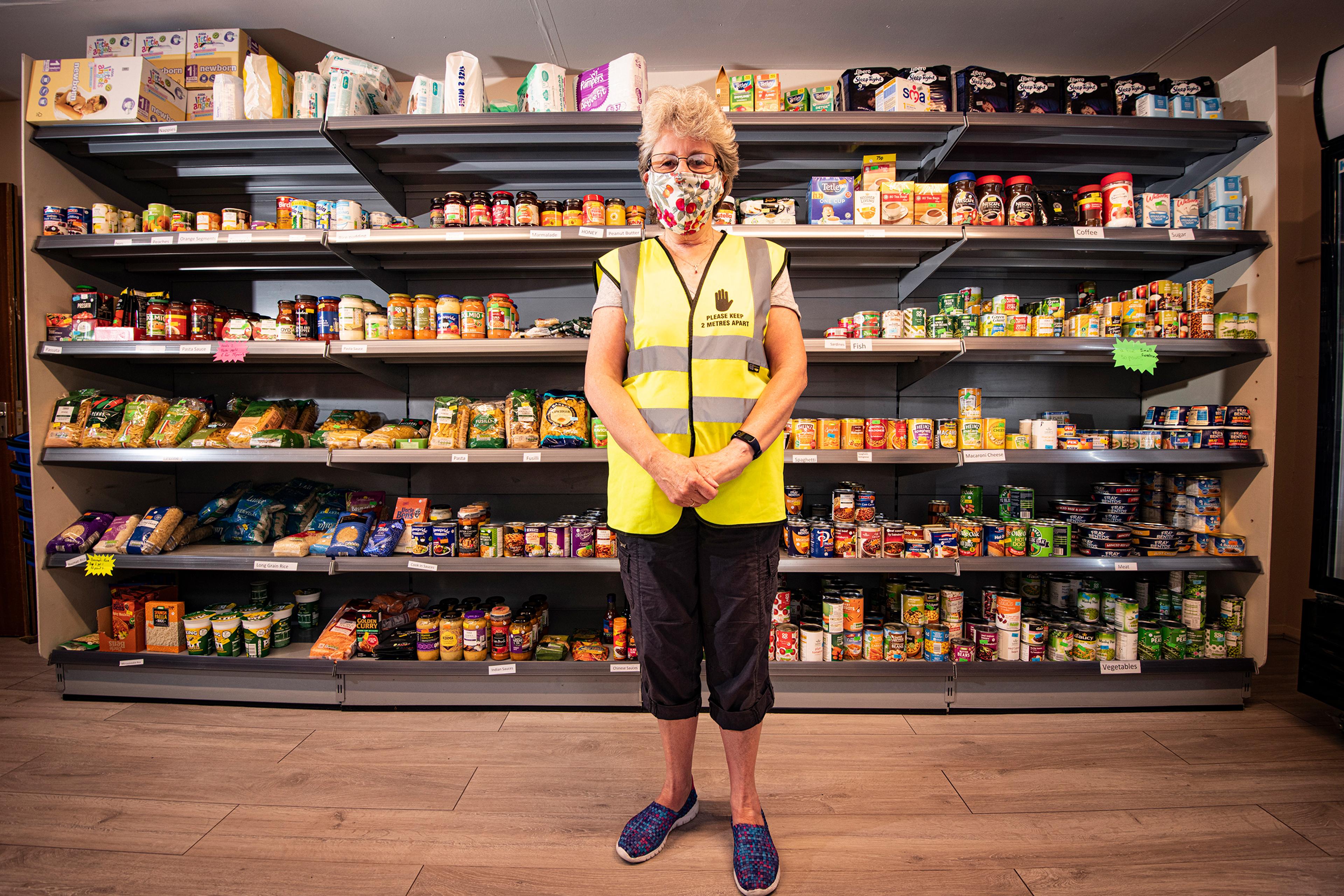 A person in a high-vis vest wearing a mask standing in front of shelves filled with food products.