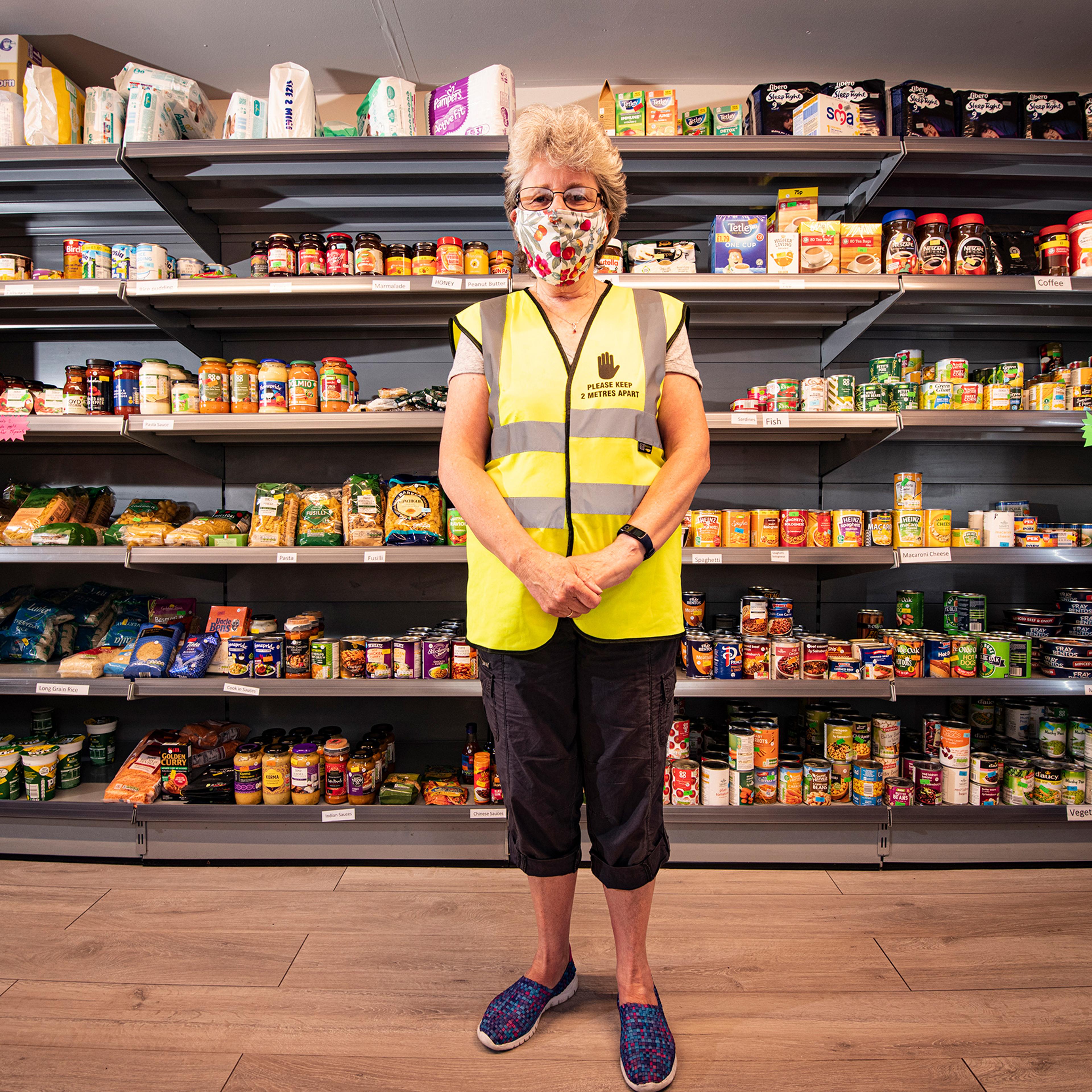 A person in a high-vis vest wearing a mask standing in front of shelves filled with food products.