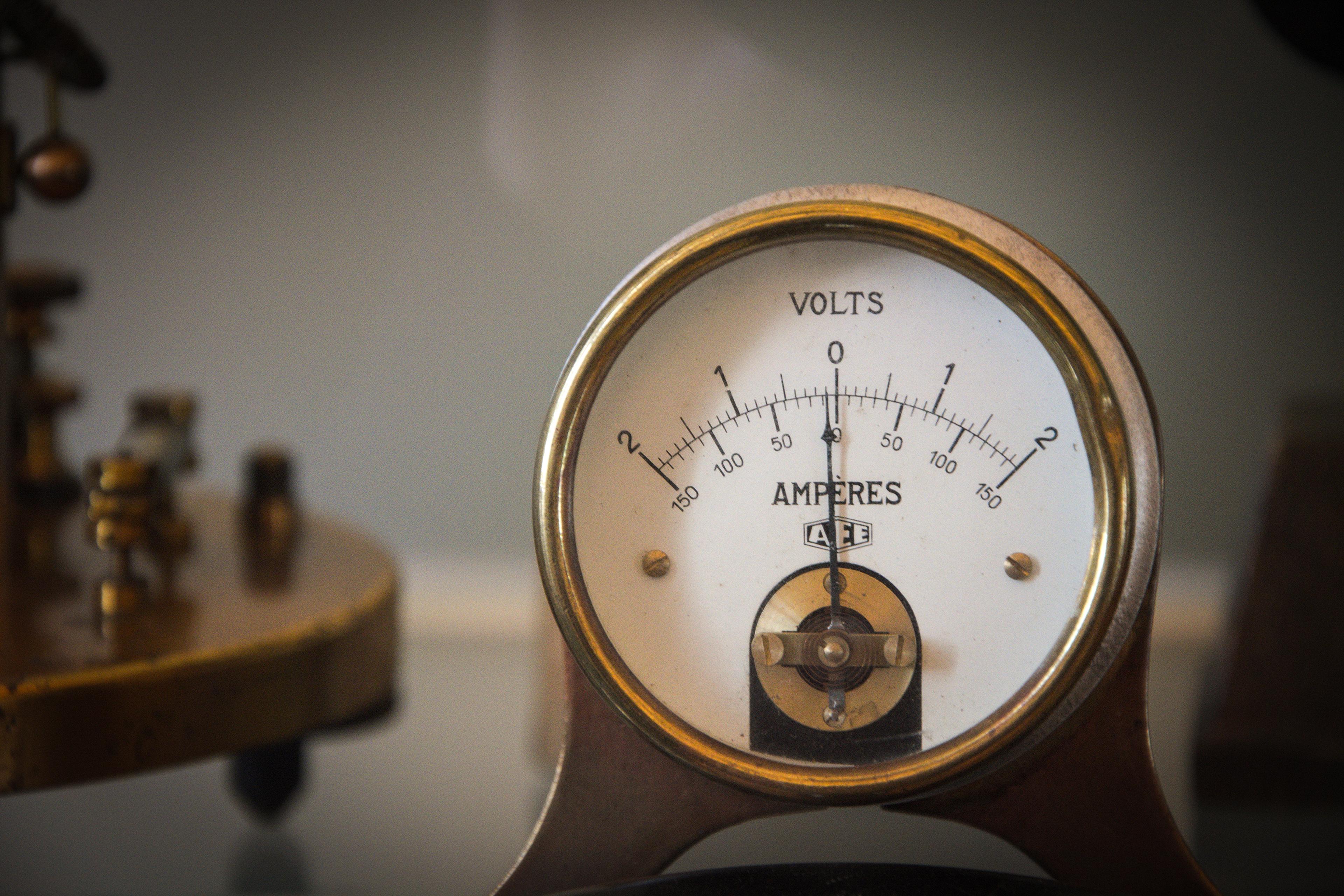 A vintage voltmeter displaying a scale in volts and ampères with a brass base and needle indicator.