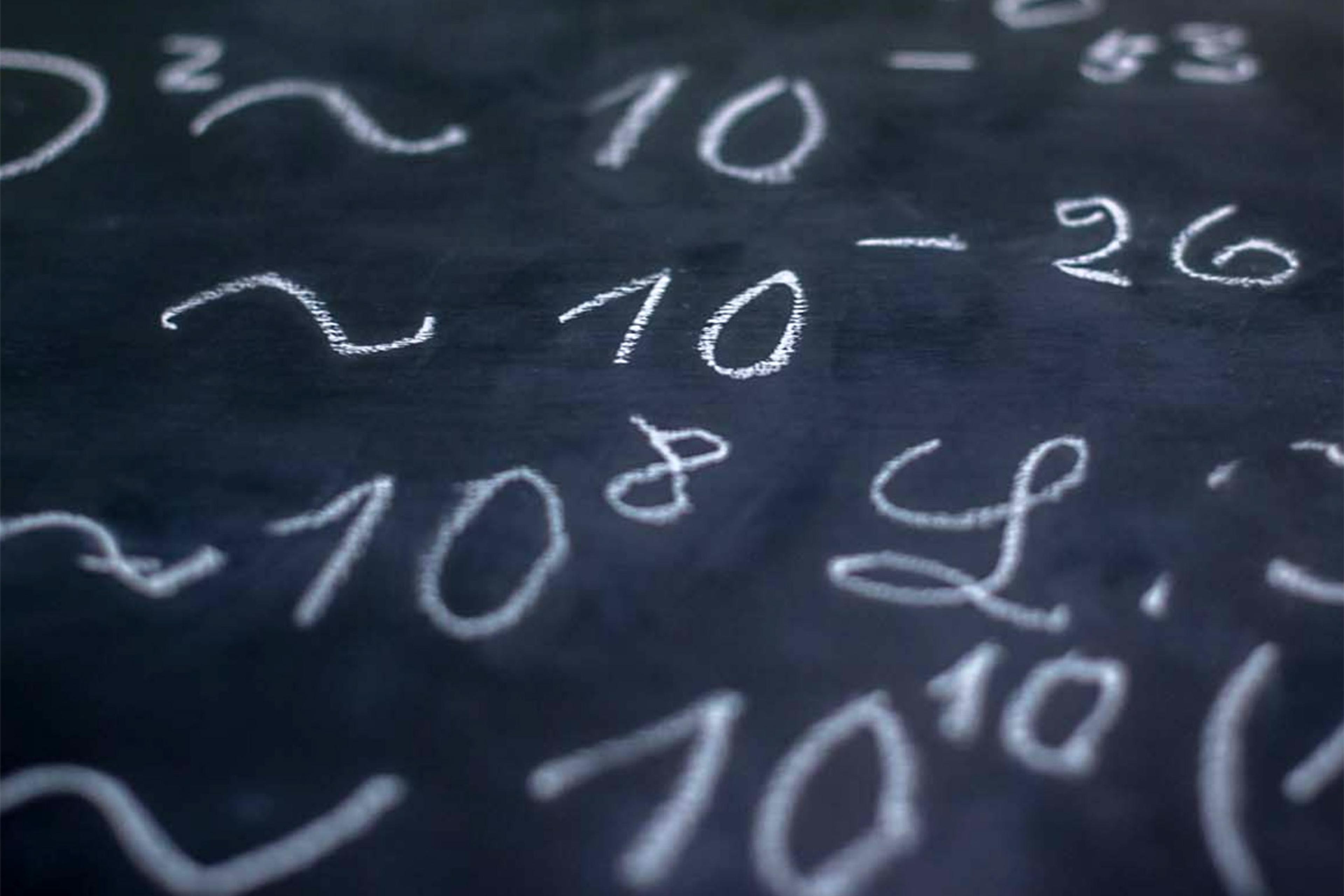 Photo of a chalkboard filled with various mathematical equations and numbers written in white chalk.