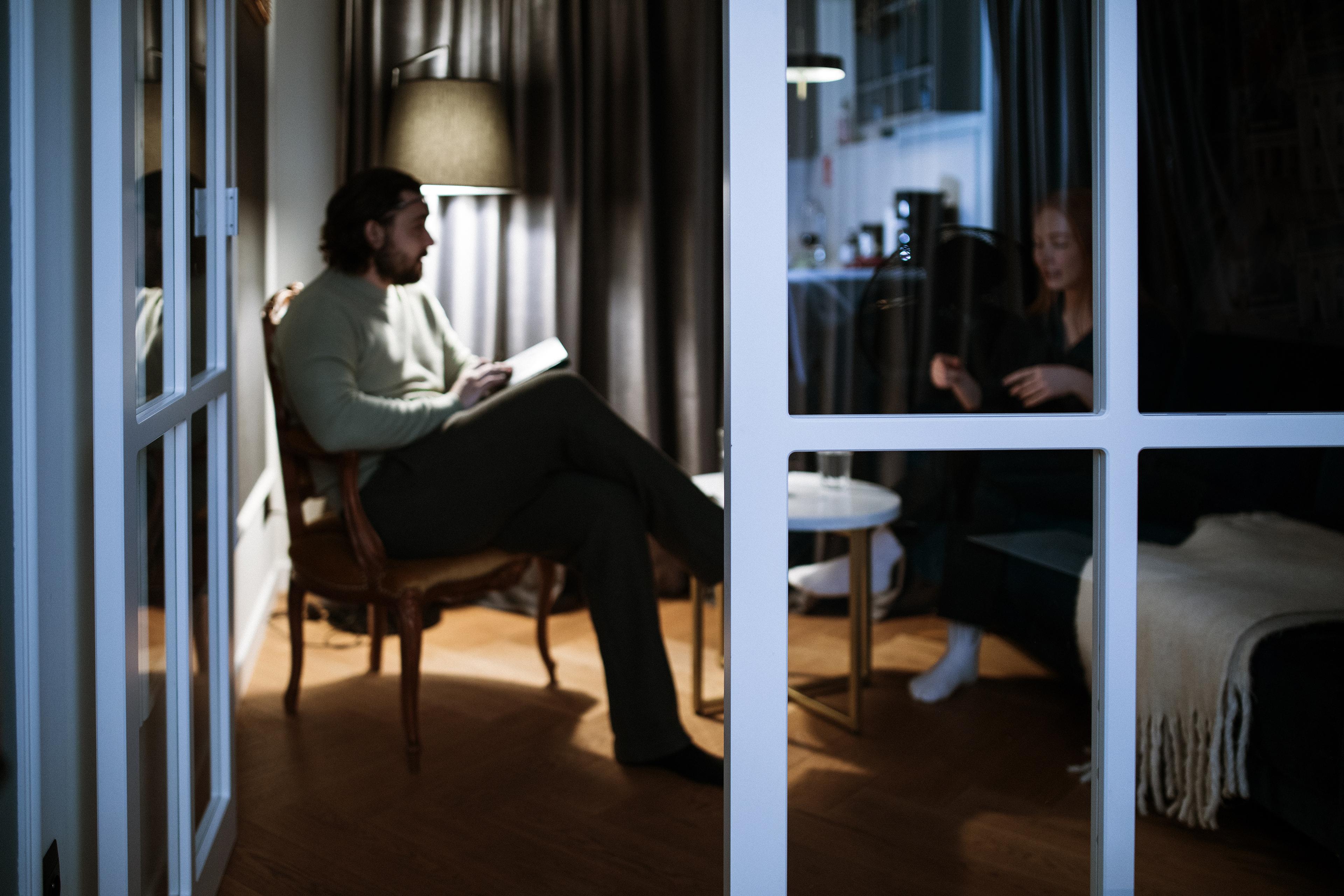 A man holding a notepad and a woman talking in a dimly lit room seen through glass doors.