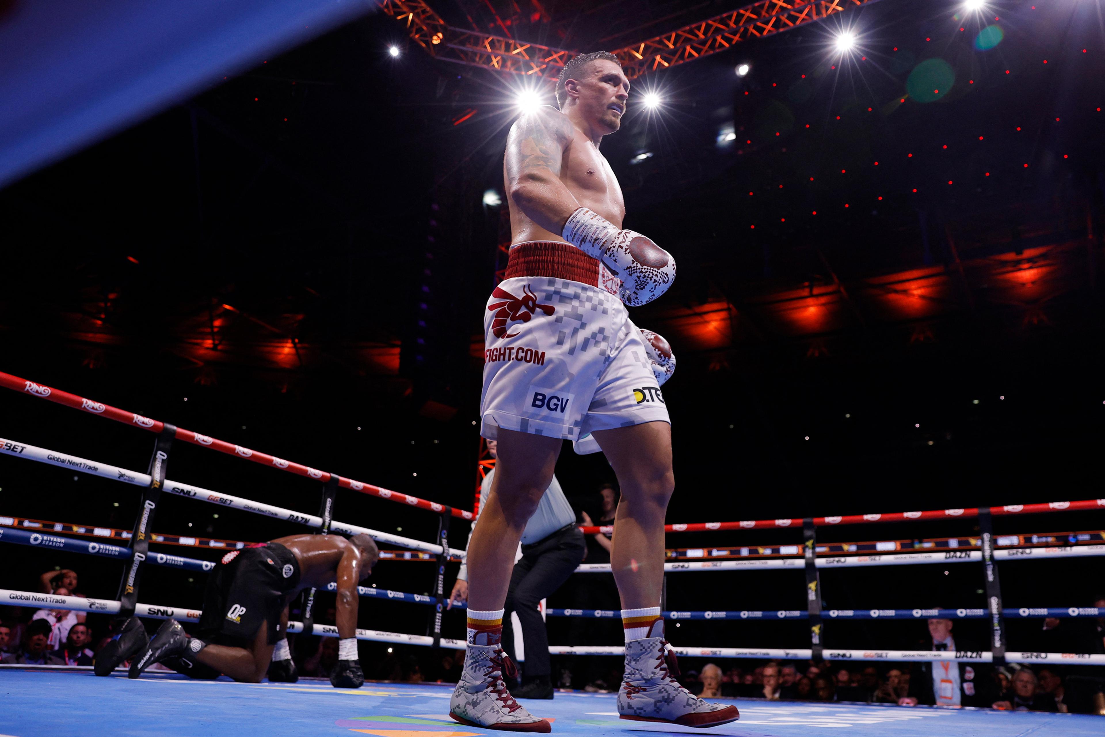 Photo of a boxing match with a standing boxer in the ring and an opponent kneeling behind, lit by overhead lights.
