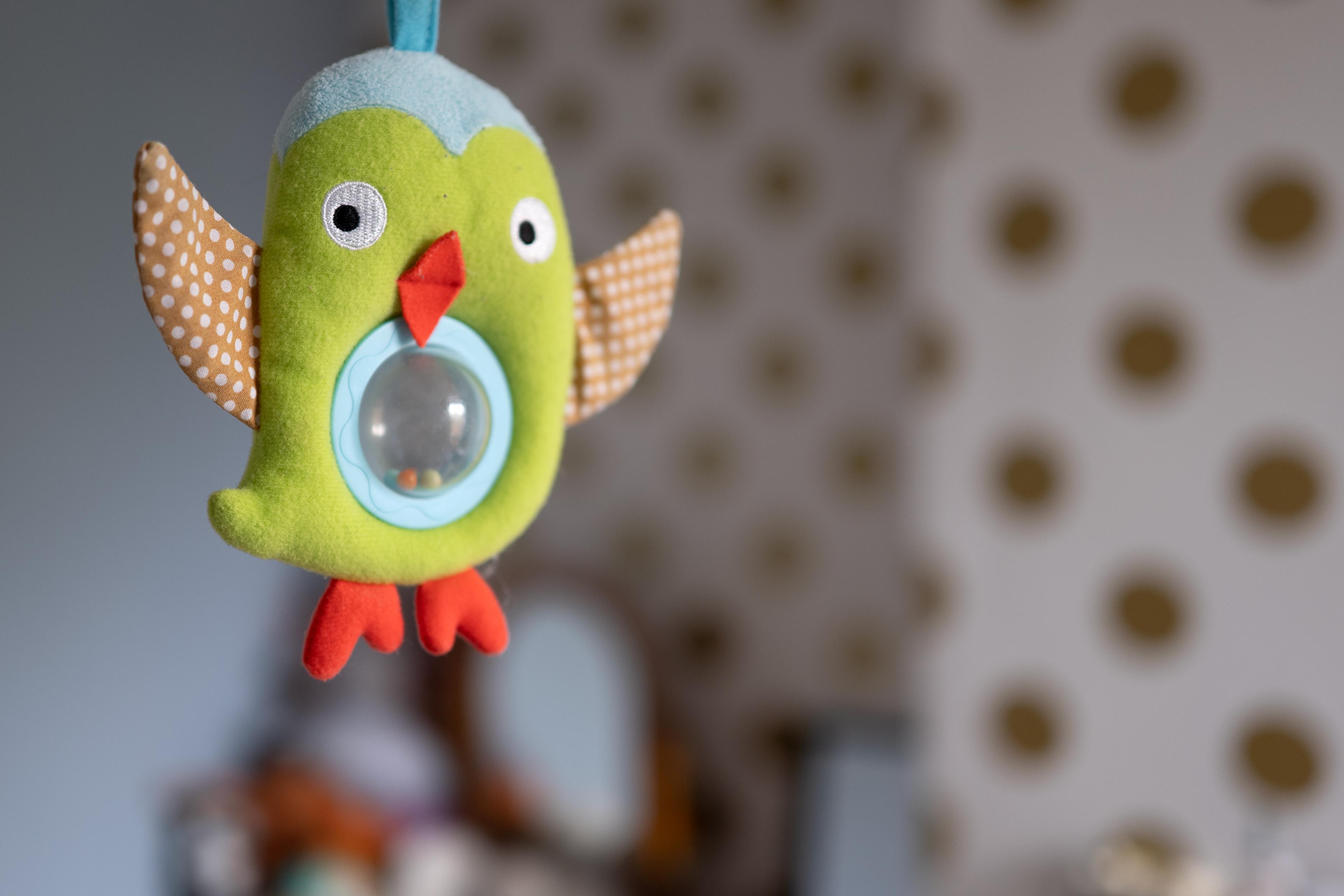 A colourful plush owl toy with polka-dot wings hanging indoors against a polka-dotted wall background.