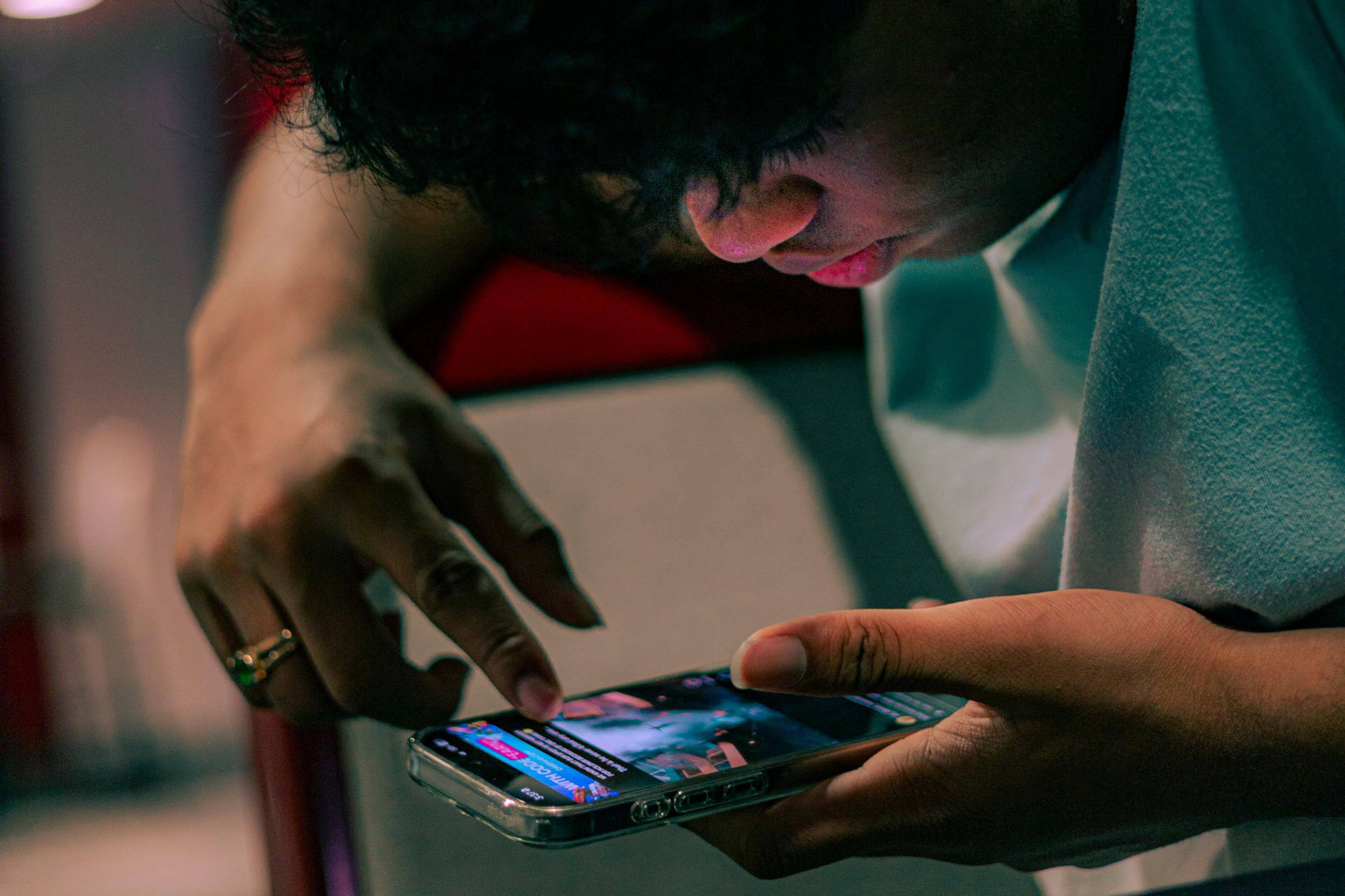 A person using a smartphone, with focus on their finger scrolling the screen. Face partially visible.
