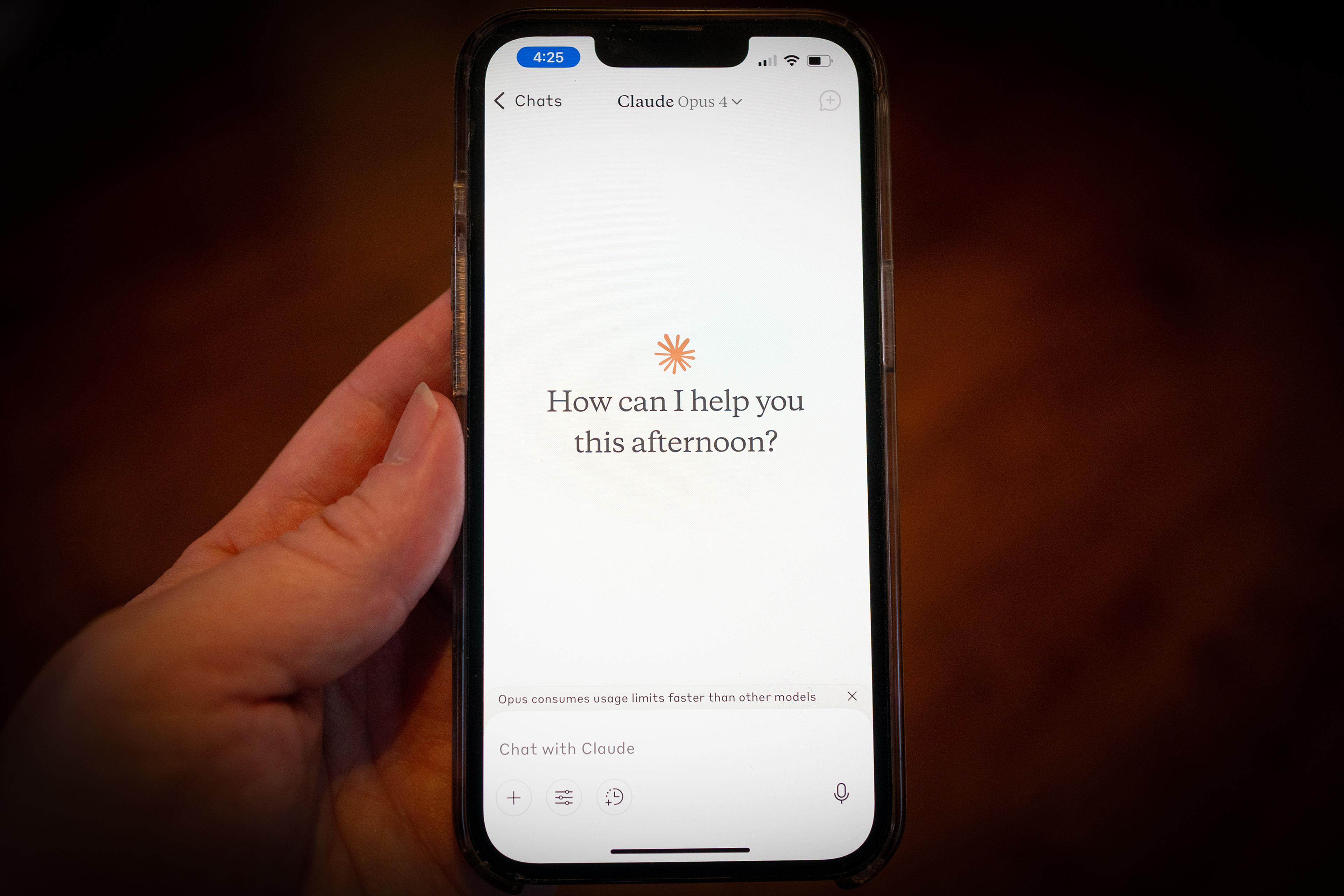 Photo of a hand holding a smartphone displaying a chat app interface asking “How can I help you this afternoon?”