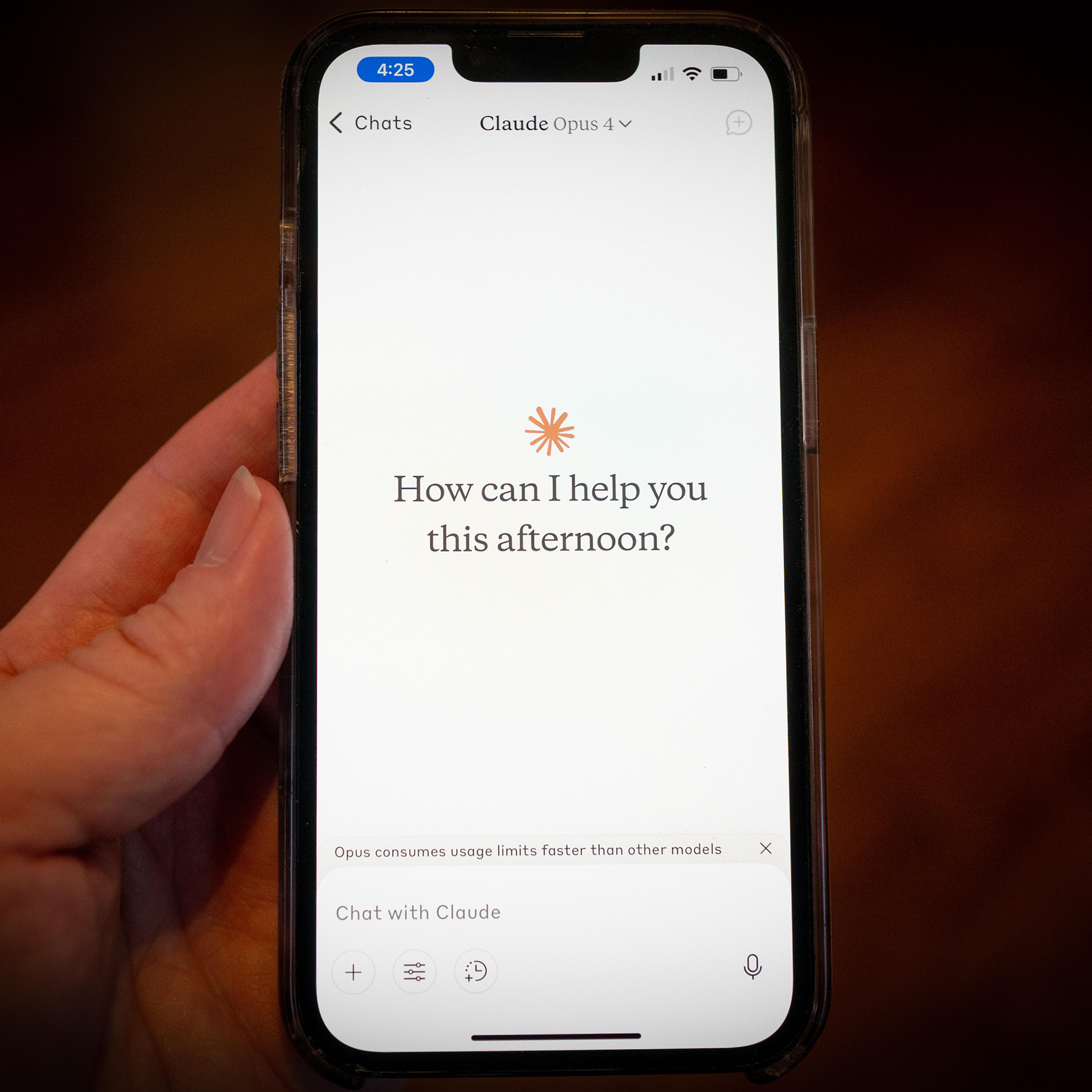 Photo of a hand holding a smartphone displaying a chat app interface asking “How can I help you this afternoon?”