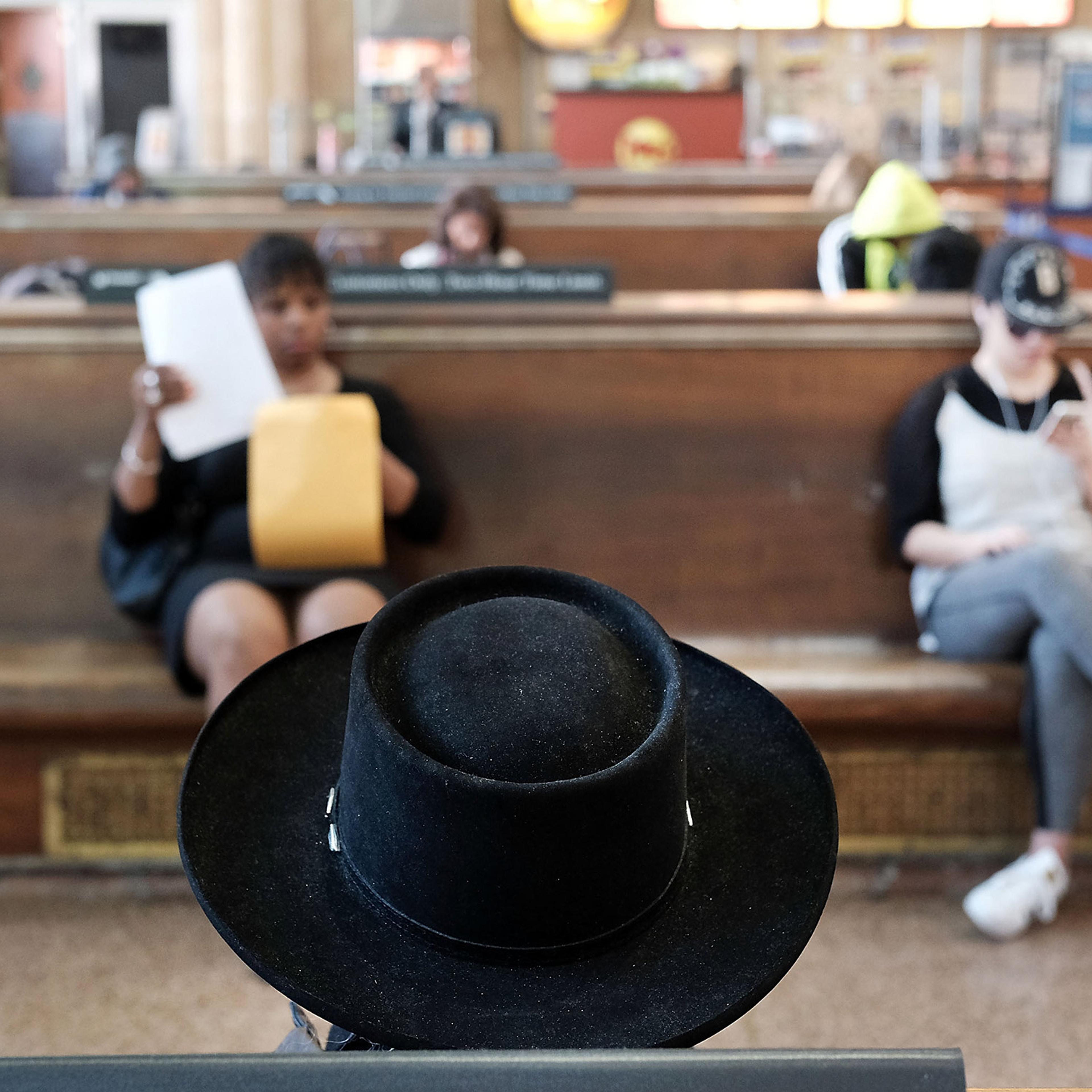 Photo of a waiting room with focus on a black hat. A woman reads papers and another looks at her phone in the background.