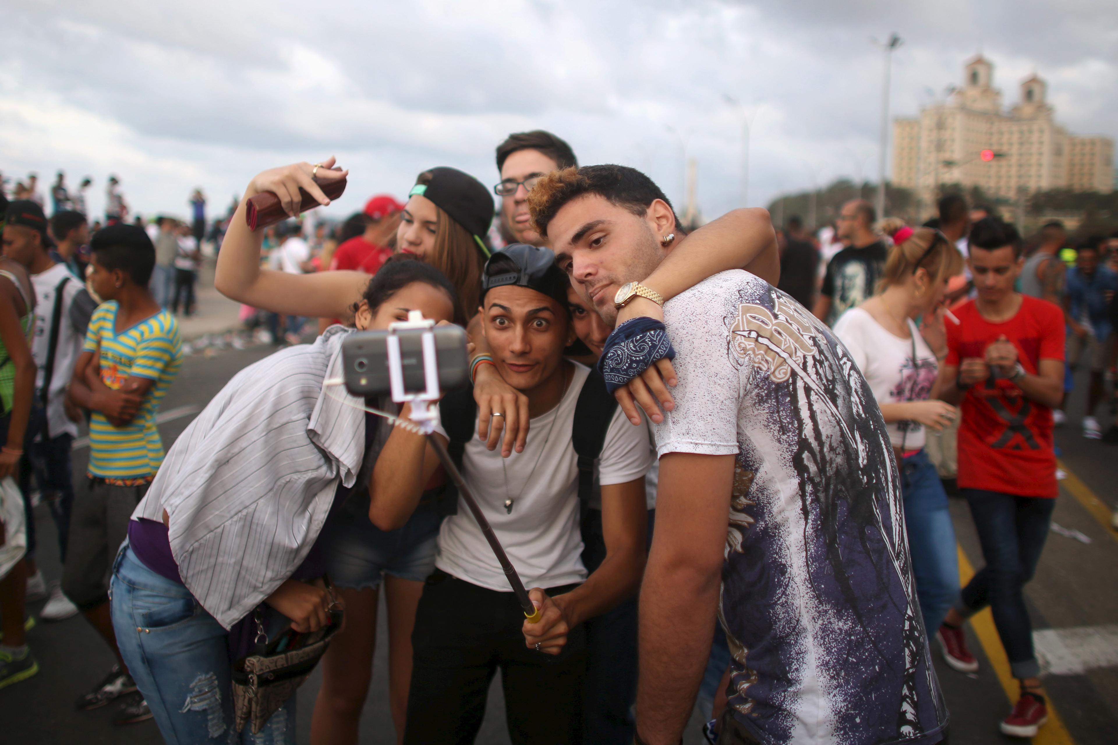 Photo of a group of young people taking a selfie with a smartphone outdoors in a busy urban setting.