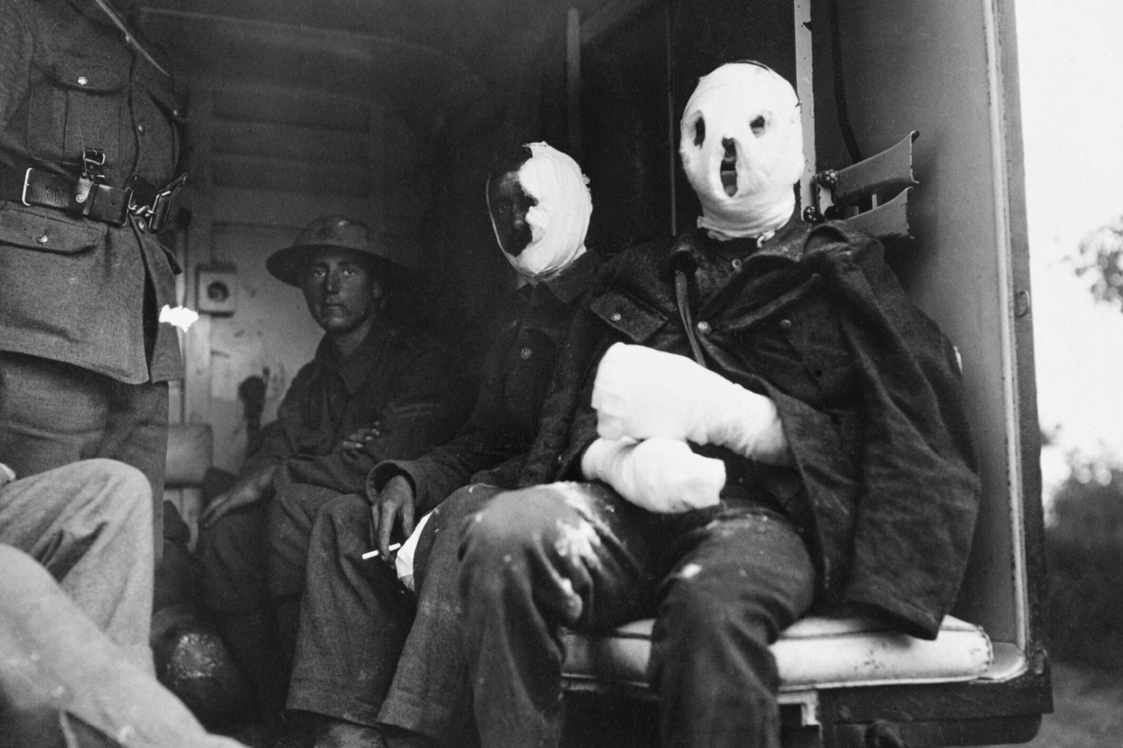 Black and white photo of soldiers in bandages sitting inside a vehicle during wartime, exhibiting visible injuries.